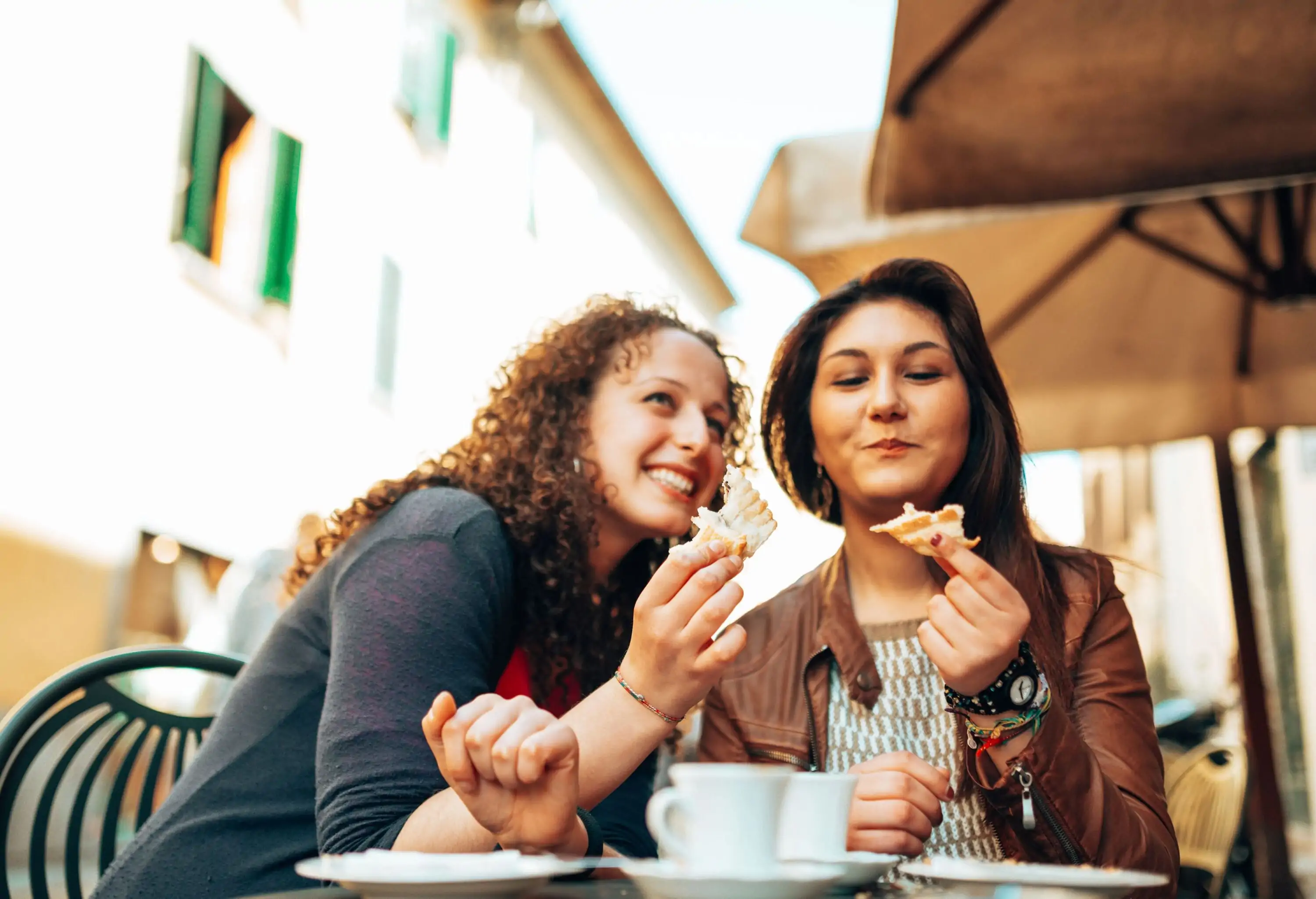 Two women enjoying coffee and pastries at an outdoor café.