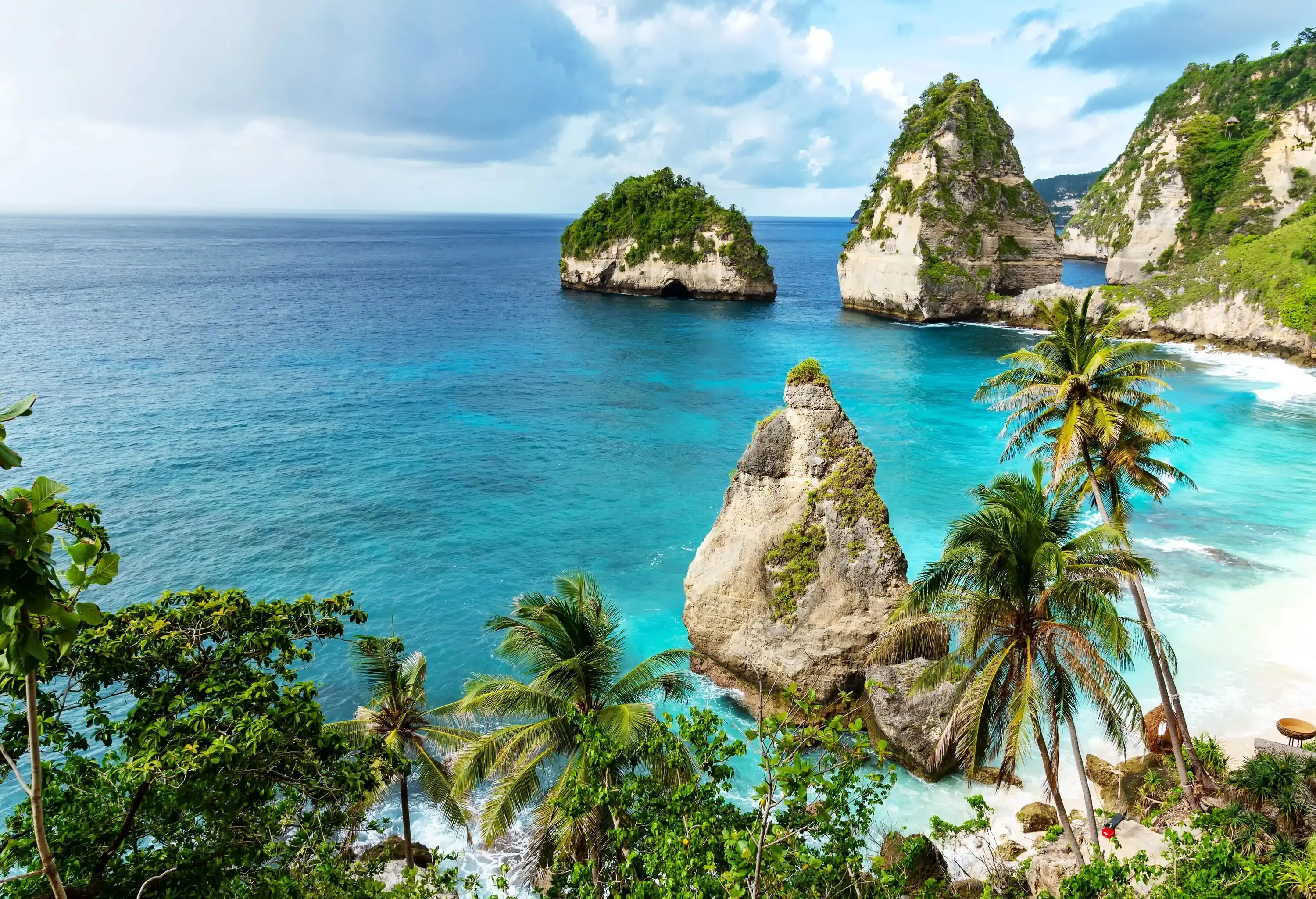 White sand beach with a vast turquoise ocean and rock formations with sharp peaks.