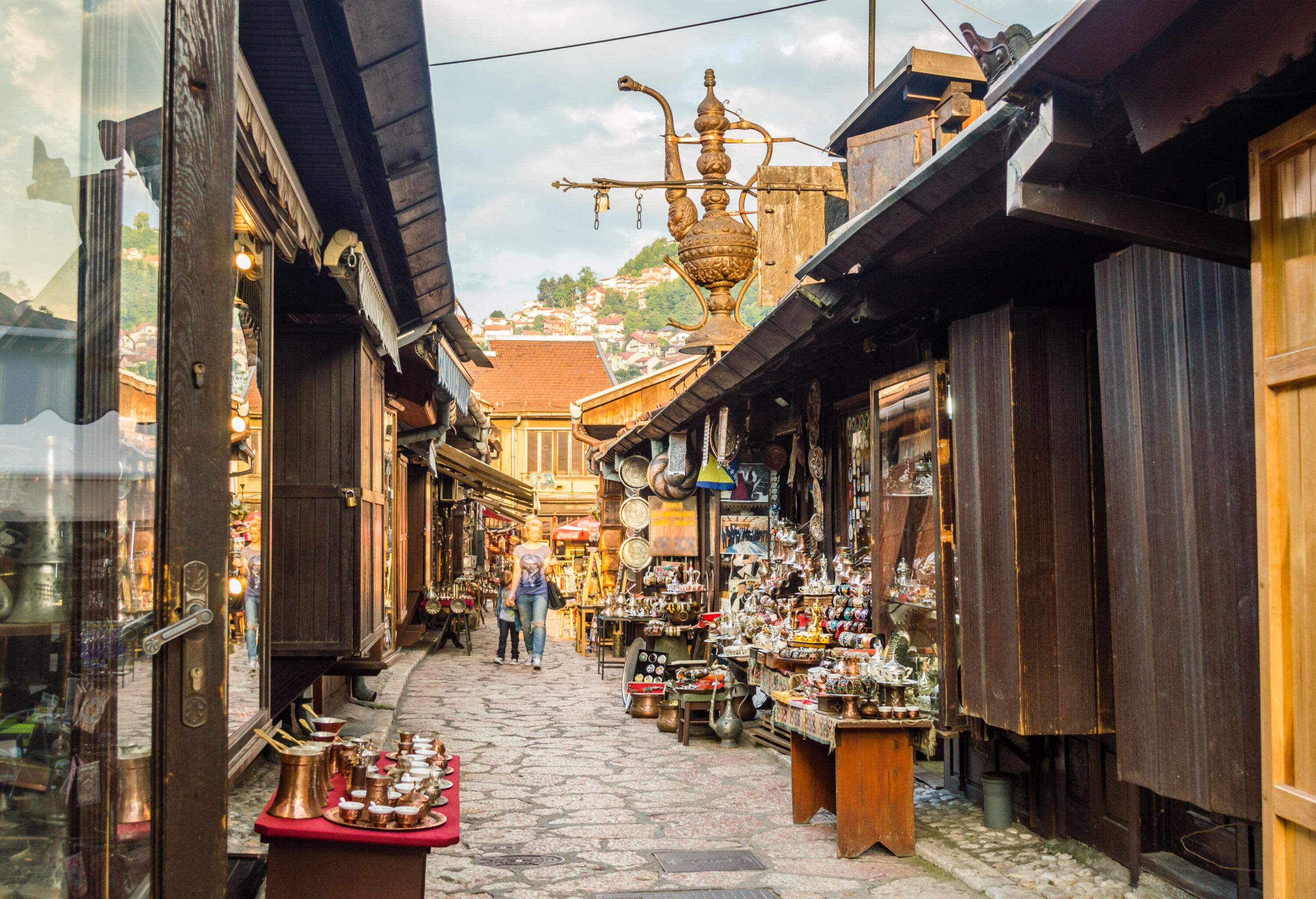 A woman looking around as she walks through a market street lined shops selling trinkets and souvenirs.