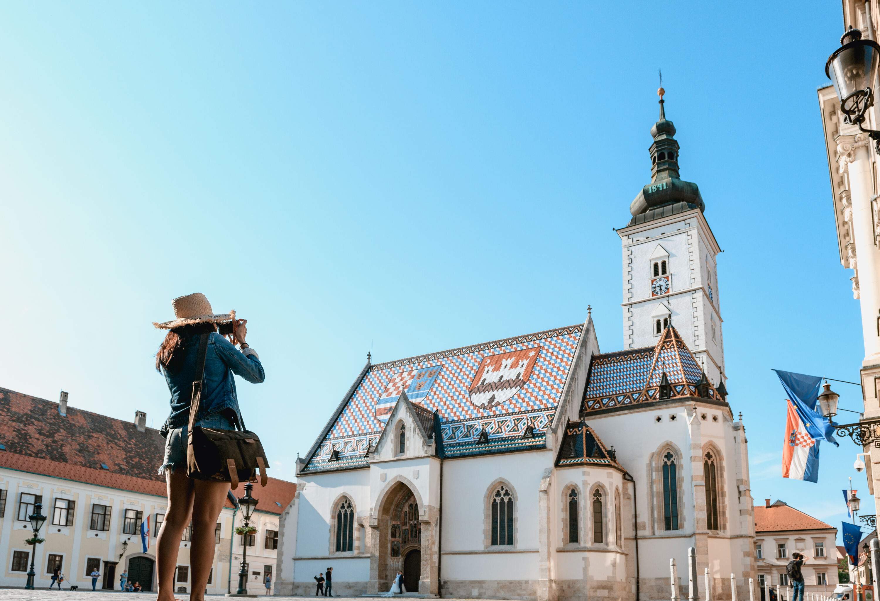 A tourist with a mobile phone taking pictures of the old parish church of St. Mark in Zagreb, Croatia.