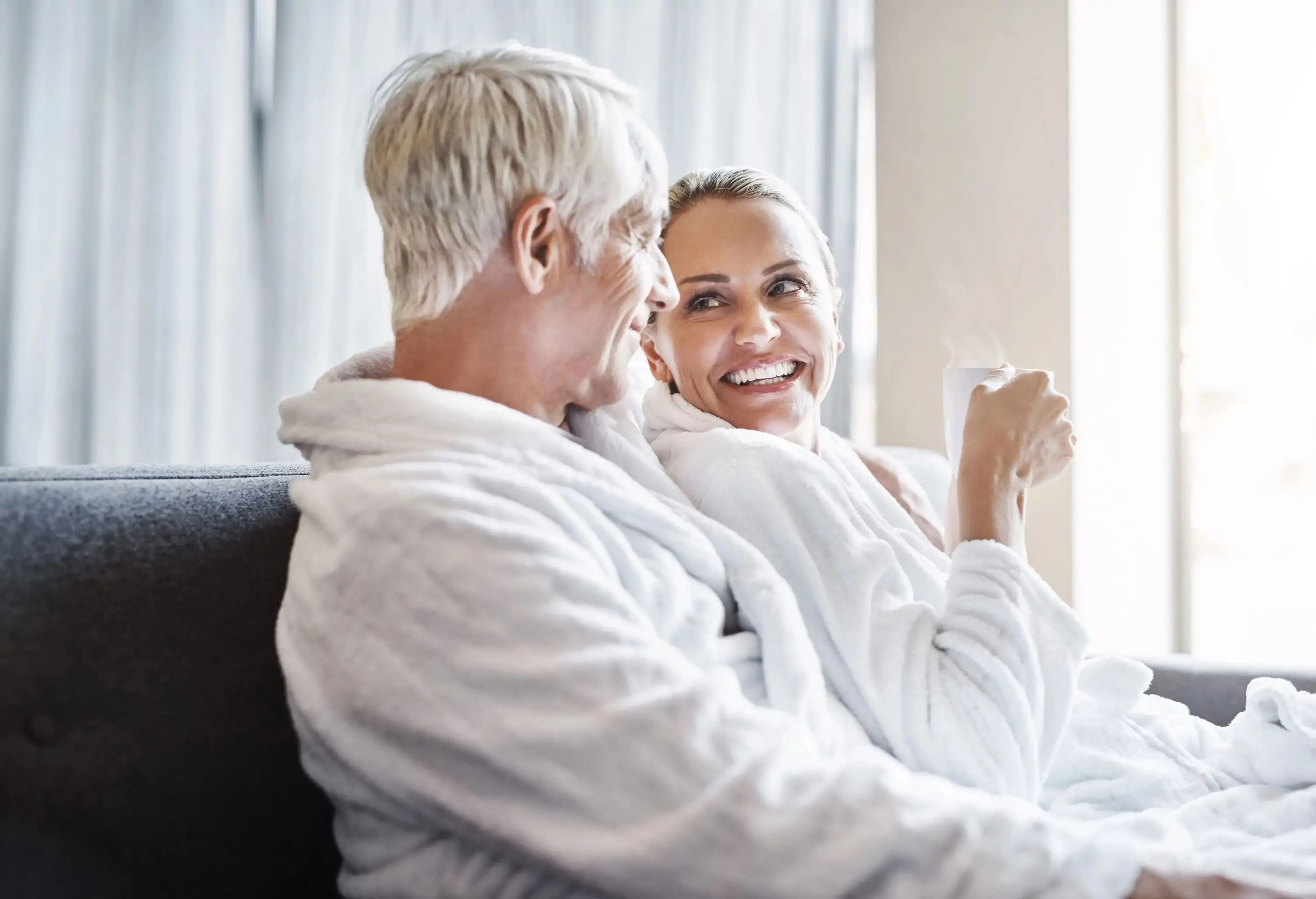 Shot of a cheerful middle aged couple relaxing together while wearing bathrobes and sitting on a couch inside of a spa during the day