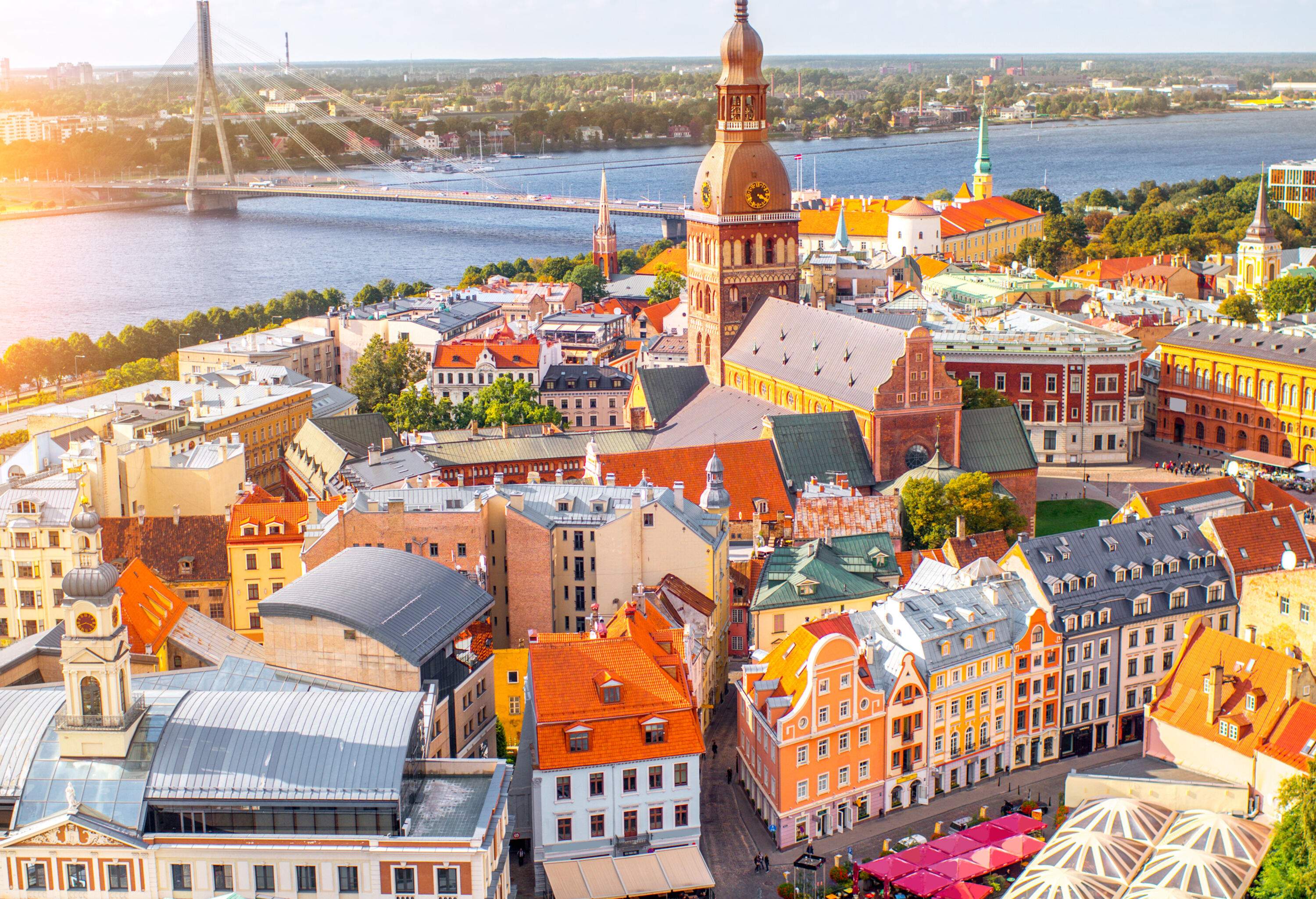 Pastel colour buildings clustered on the river bank dominated by a church tower accessed through a bridge.