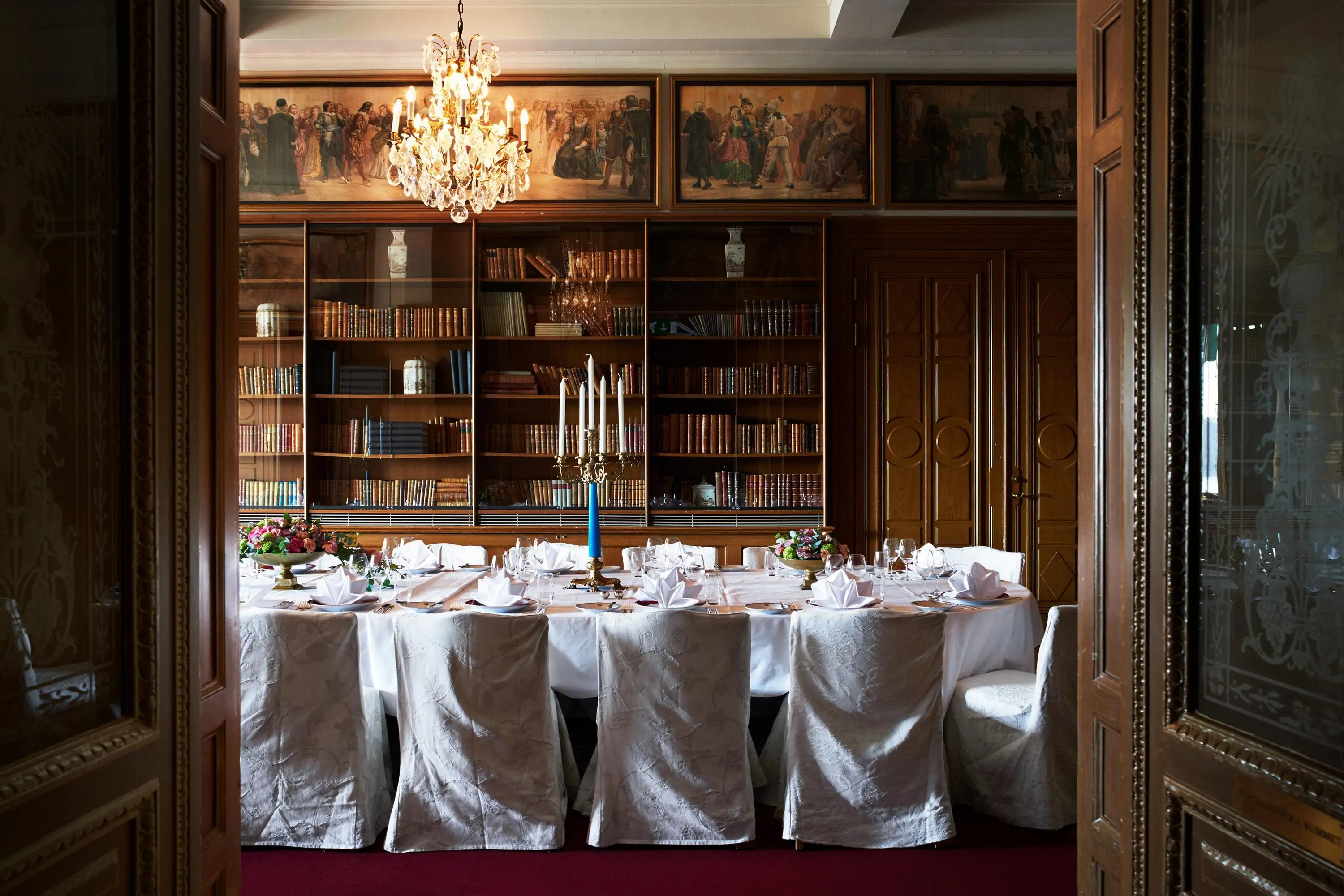 Interior view of a table set with white soft furnishings by an antique library