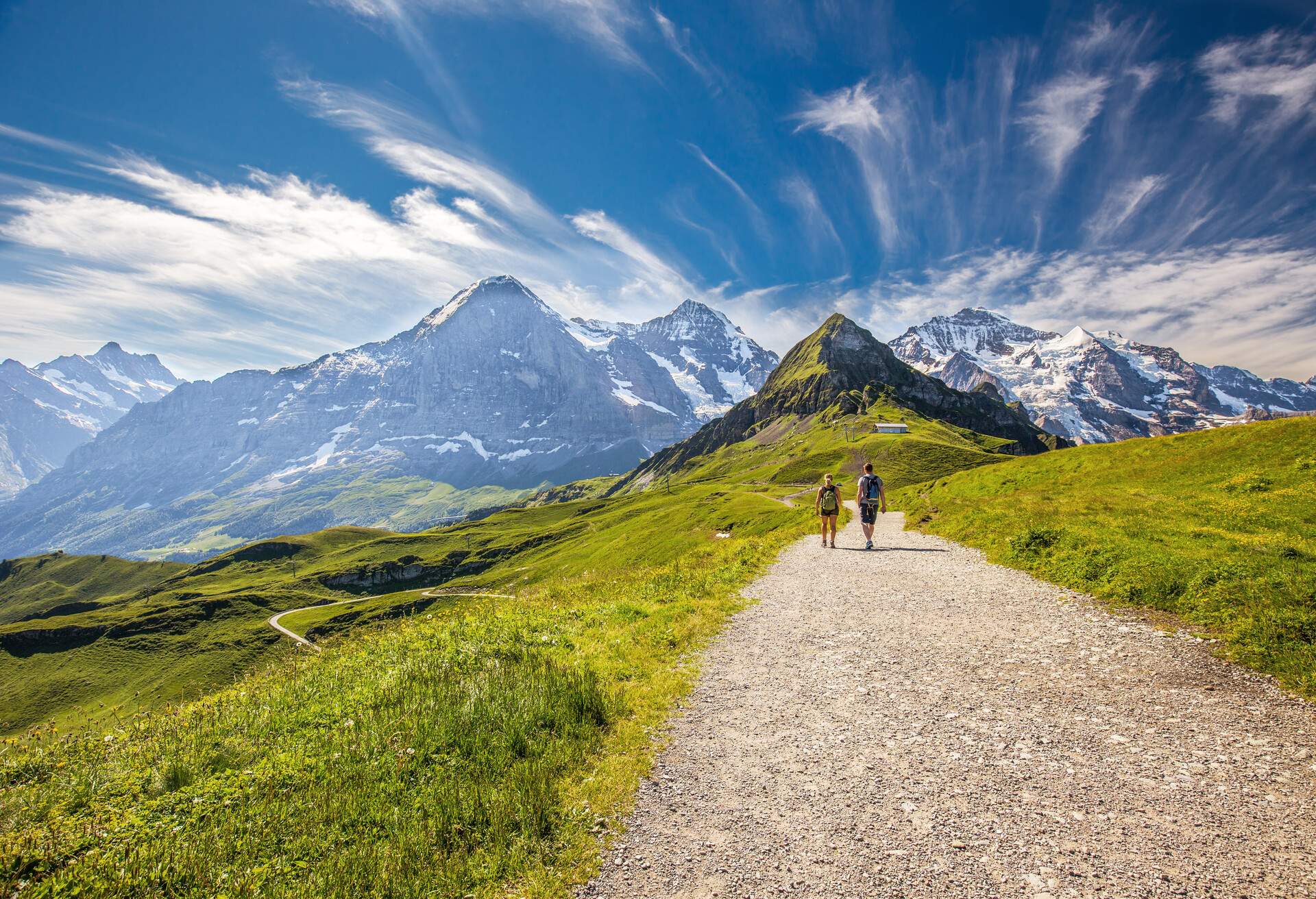 Young couple hiking in panorama trail leading to Kleine Scheidegg from Mannlichen with Eiger, Monch and Jungfrau mountain (Swiss Alps) in the background, Berner Oberland, Grindelwald, Switzerland