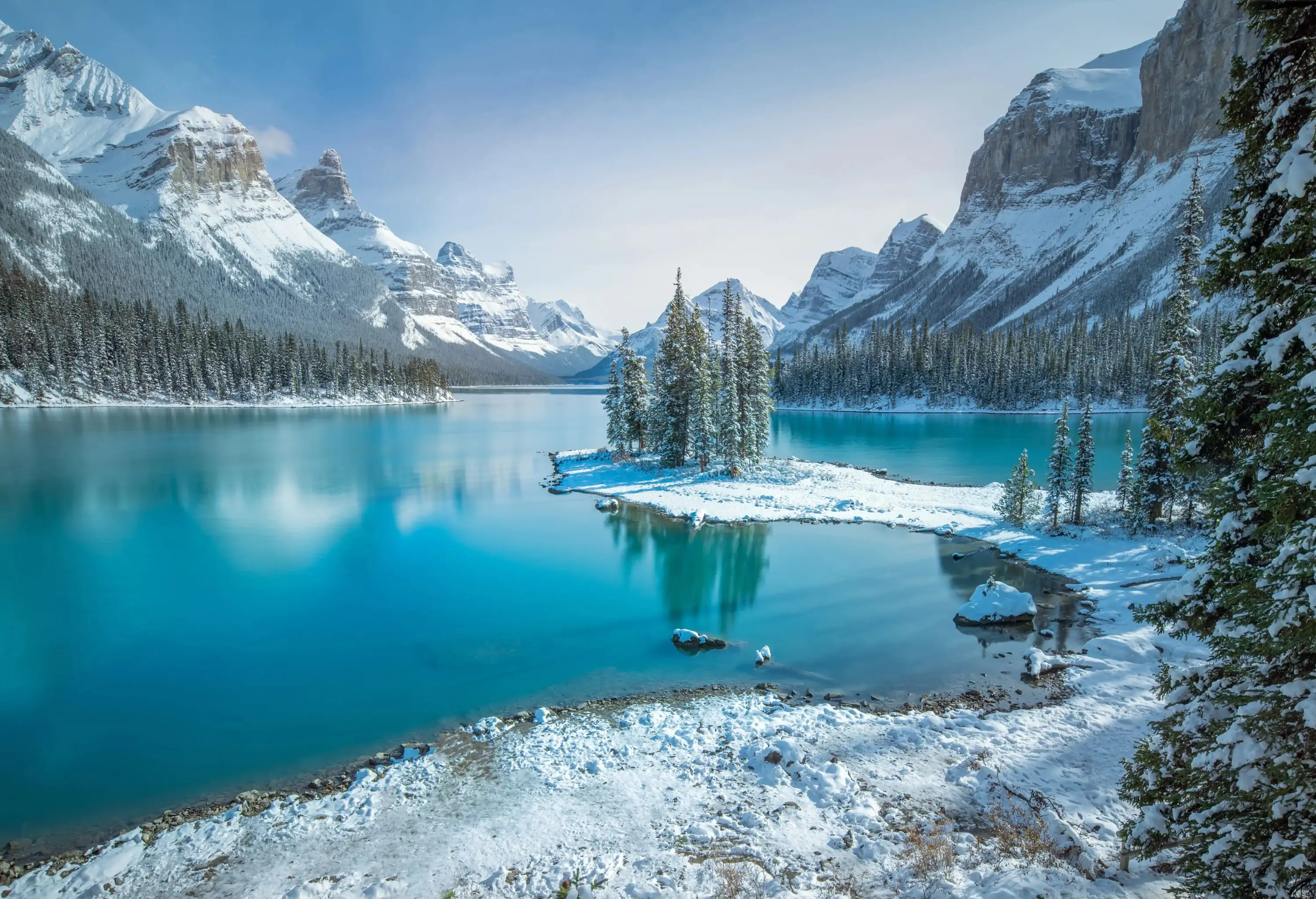 A picturesque turquoise glacial lake enclosed by lush cypress trees and breathtaking snow-capped steep mountains.