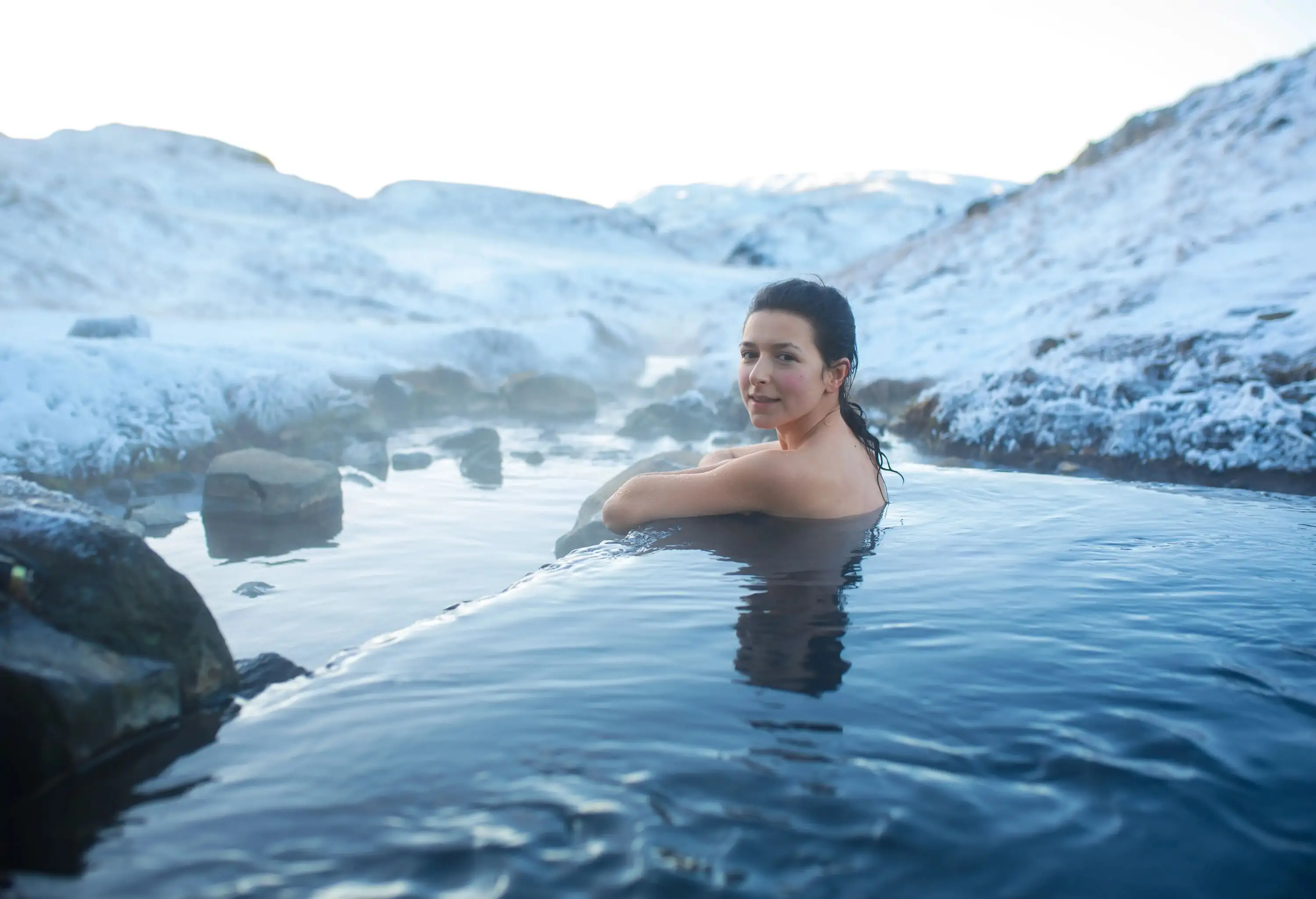 Woman bathes in a hot spring in the open air with view of the snowy mountains in winter.