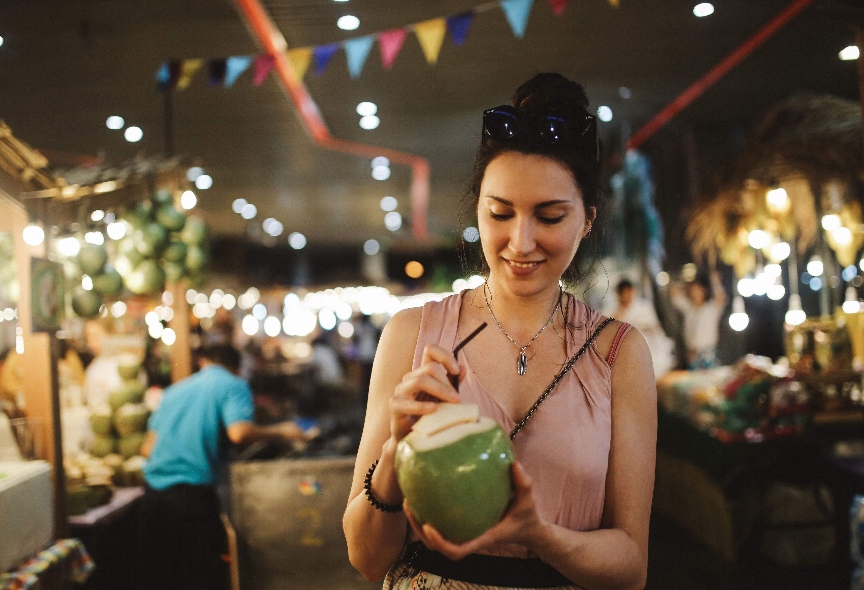 A woman slipping a straw into a coconut while standing inside a market.