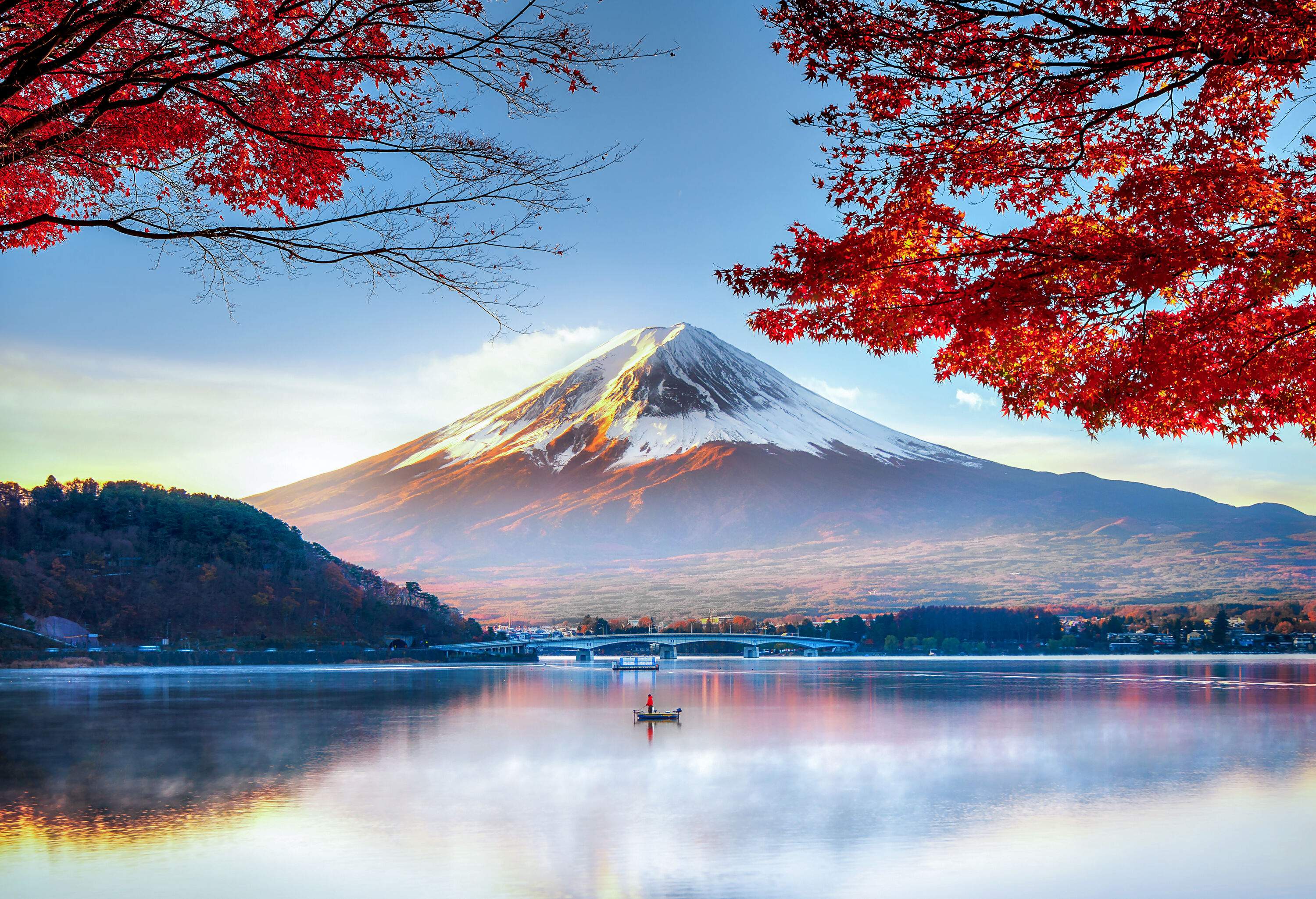 An individual on a scenic lake reflecting autumn's vibrant colours with a view of the awe-inspiring beauty of the snow-capped Mount Fuji in Japan. 