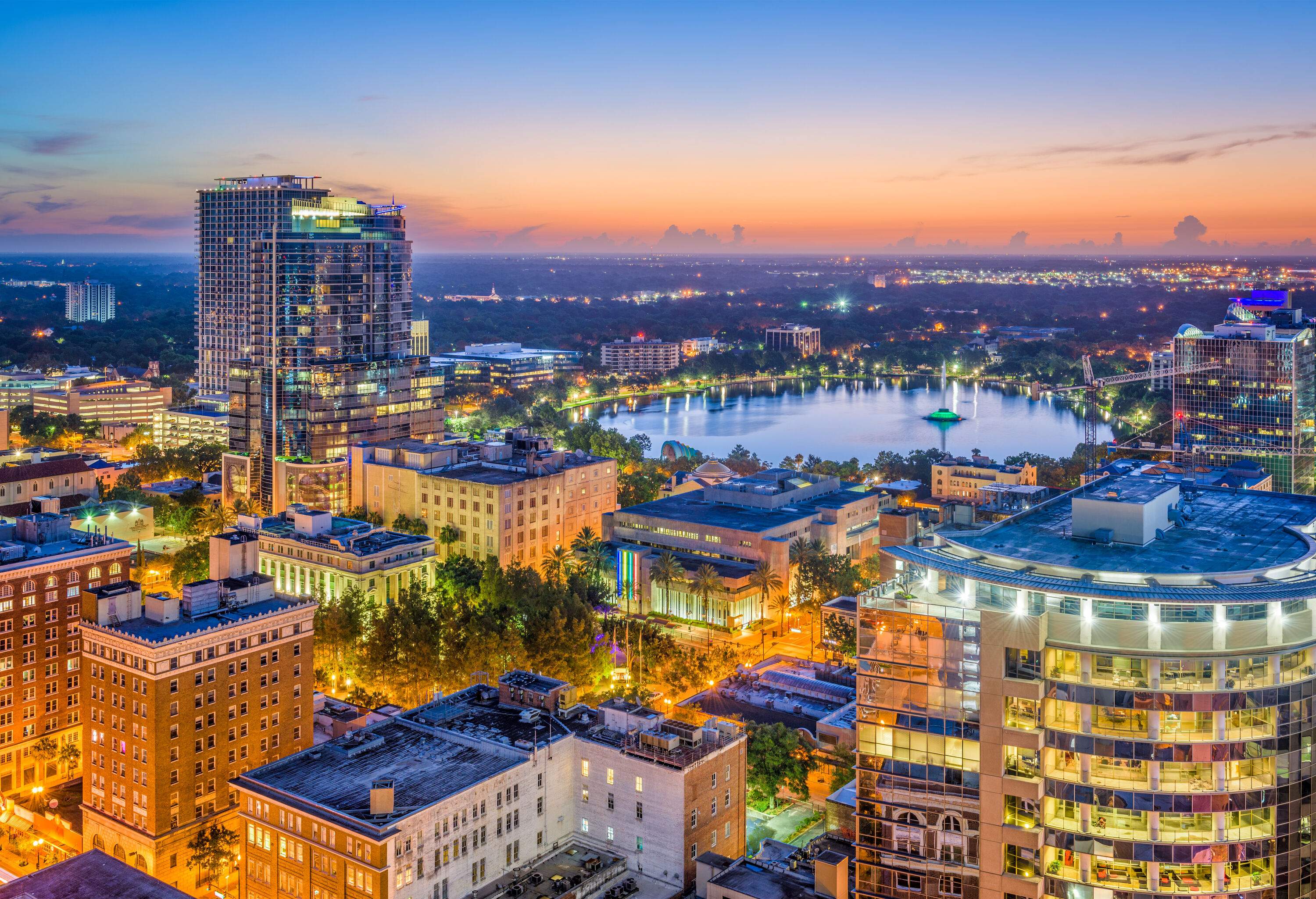 Skyline of colourfully lit urban cityscape with modern buildings and skyscrapers and a lake in the centre at twilight.