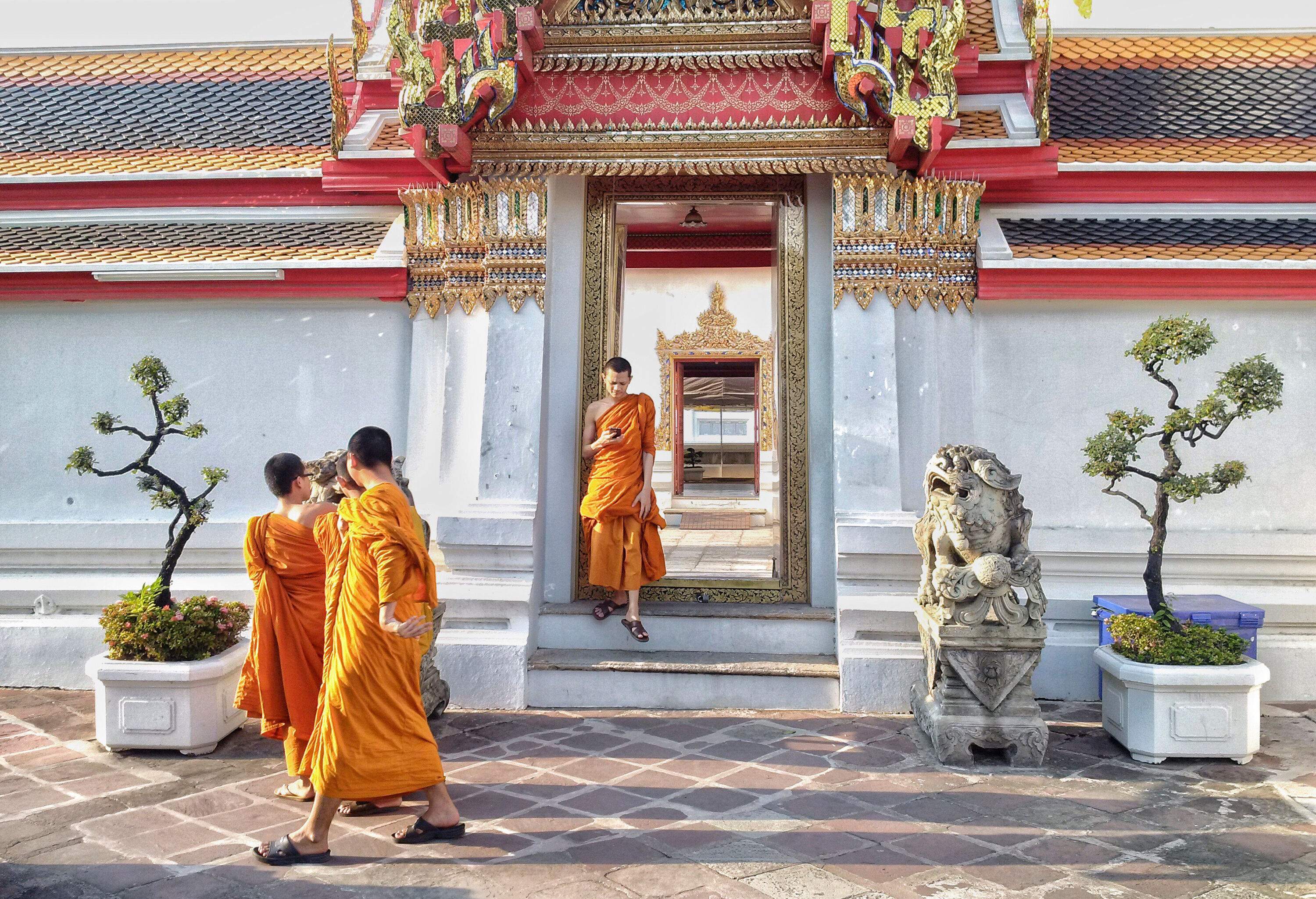 Monks standing outside a temple, one on his phone leaning against the doorway and three others on the pavement.