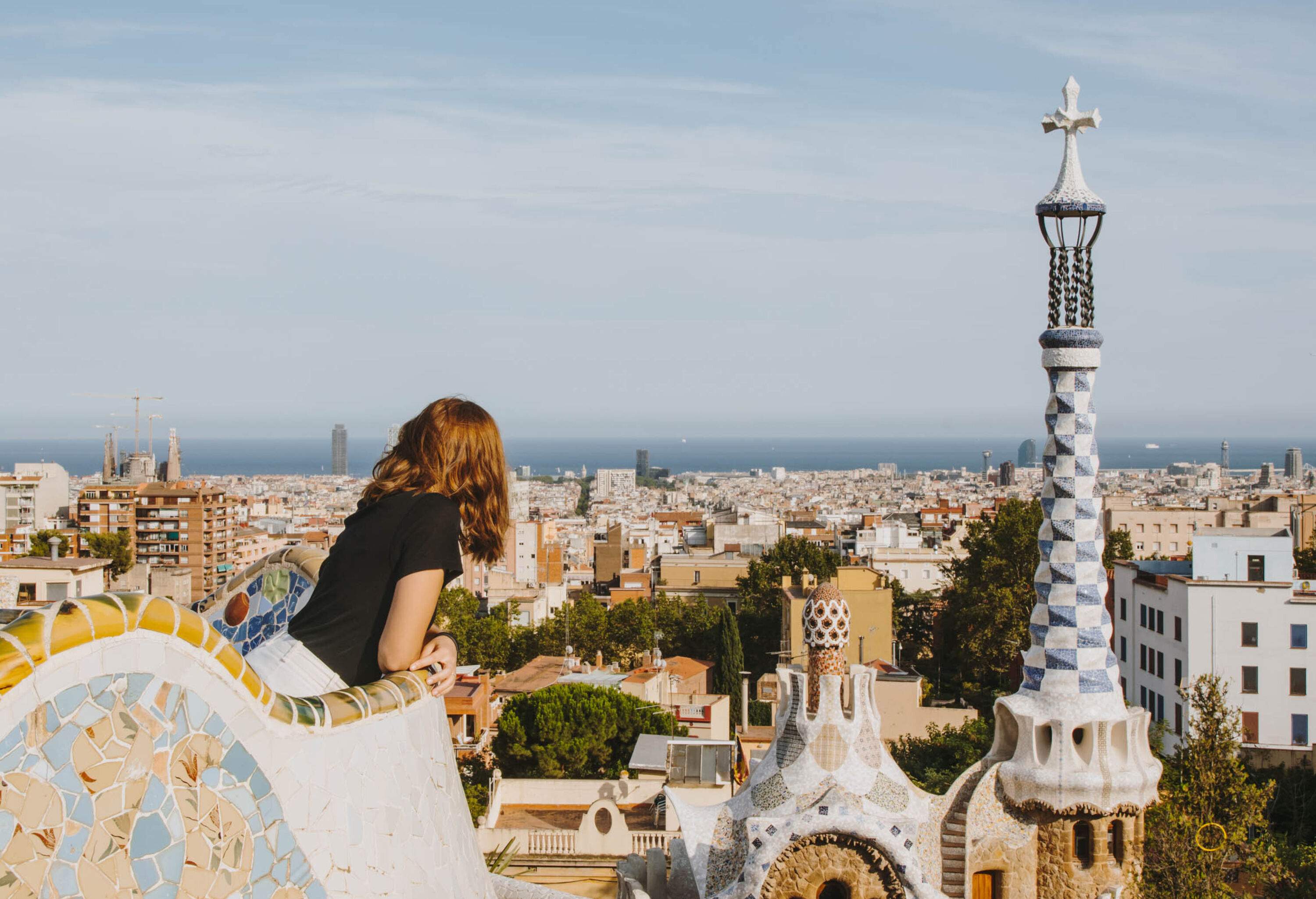 A person leans against the secure railing of a rooftop, gazing out over a sprawling cityscape.