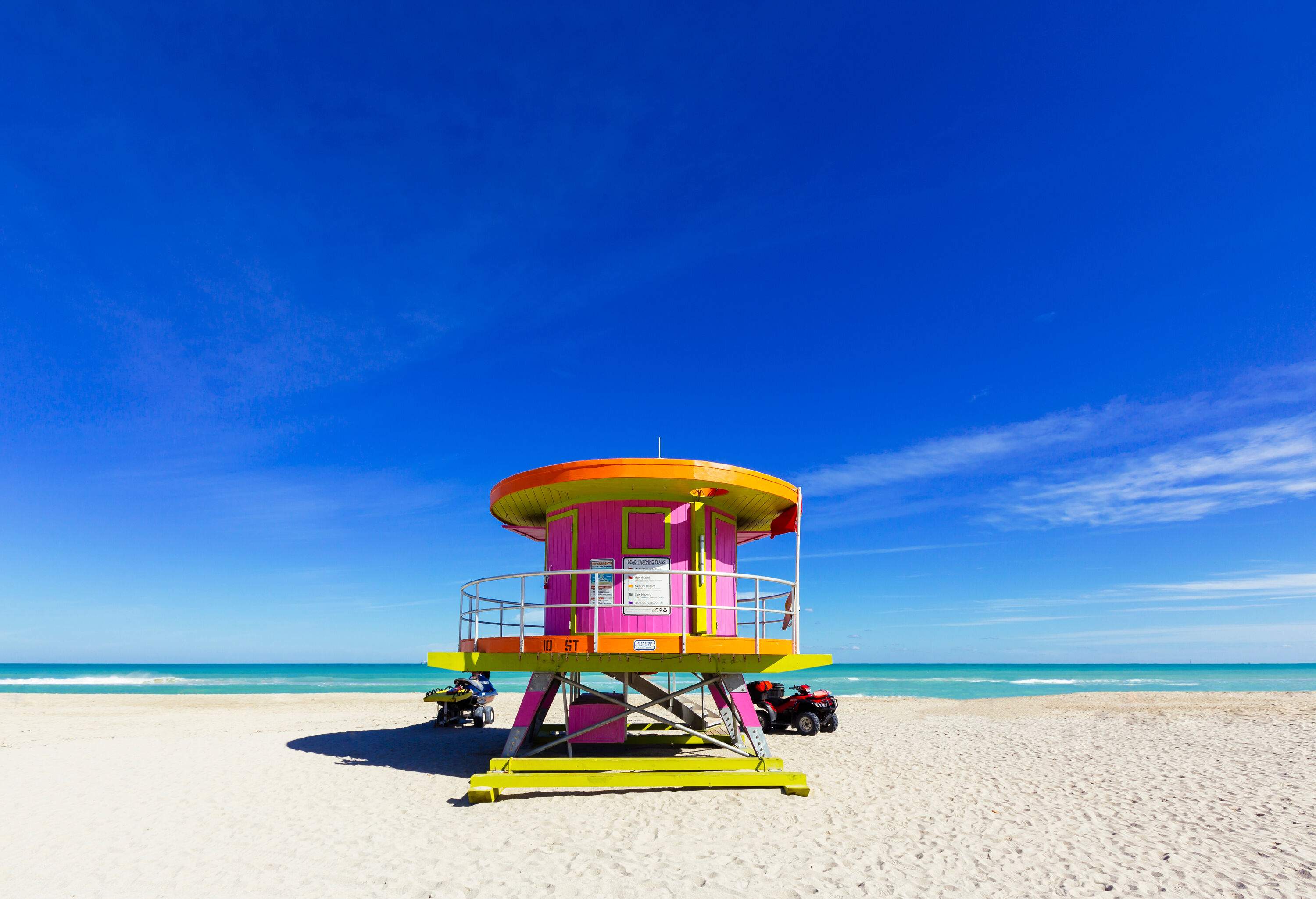 A lifeguard tower painted in vibrant colours nestled in an empty sandy beach against the clear blue sky.