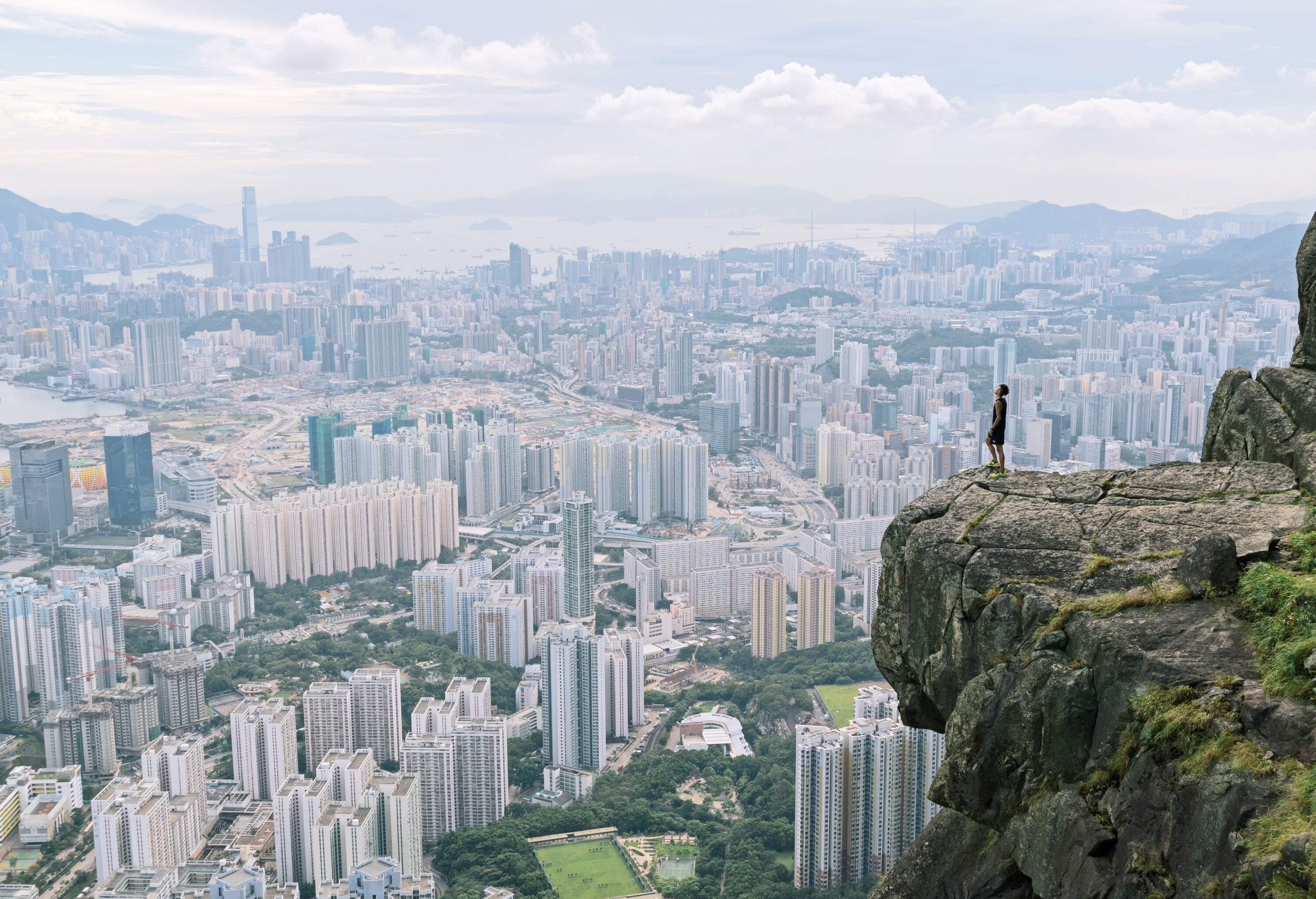 Person stands on a rock cliff with overlooking views of the city's high-rise buildings.