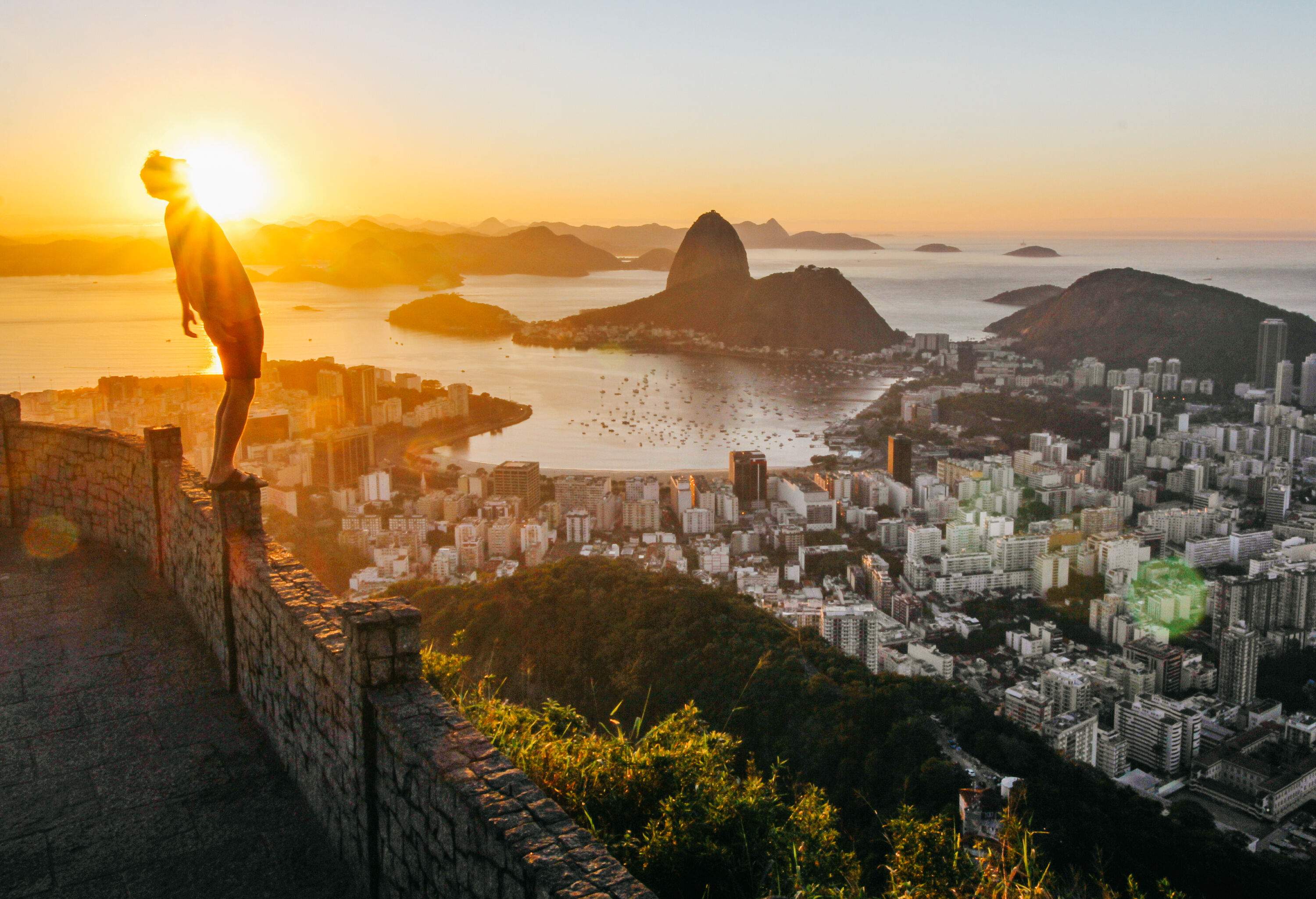 A person stands on the parapet while bathed in the warm glow of the setting sun, overlooking the vast cityscape below.