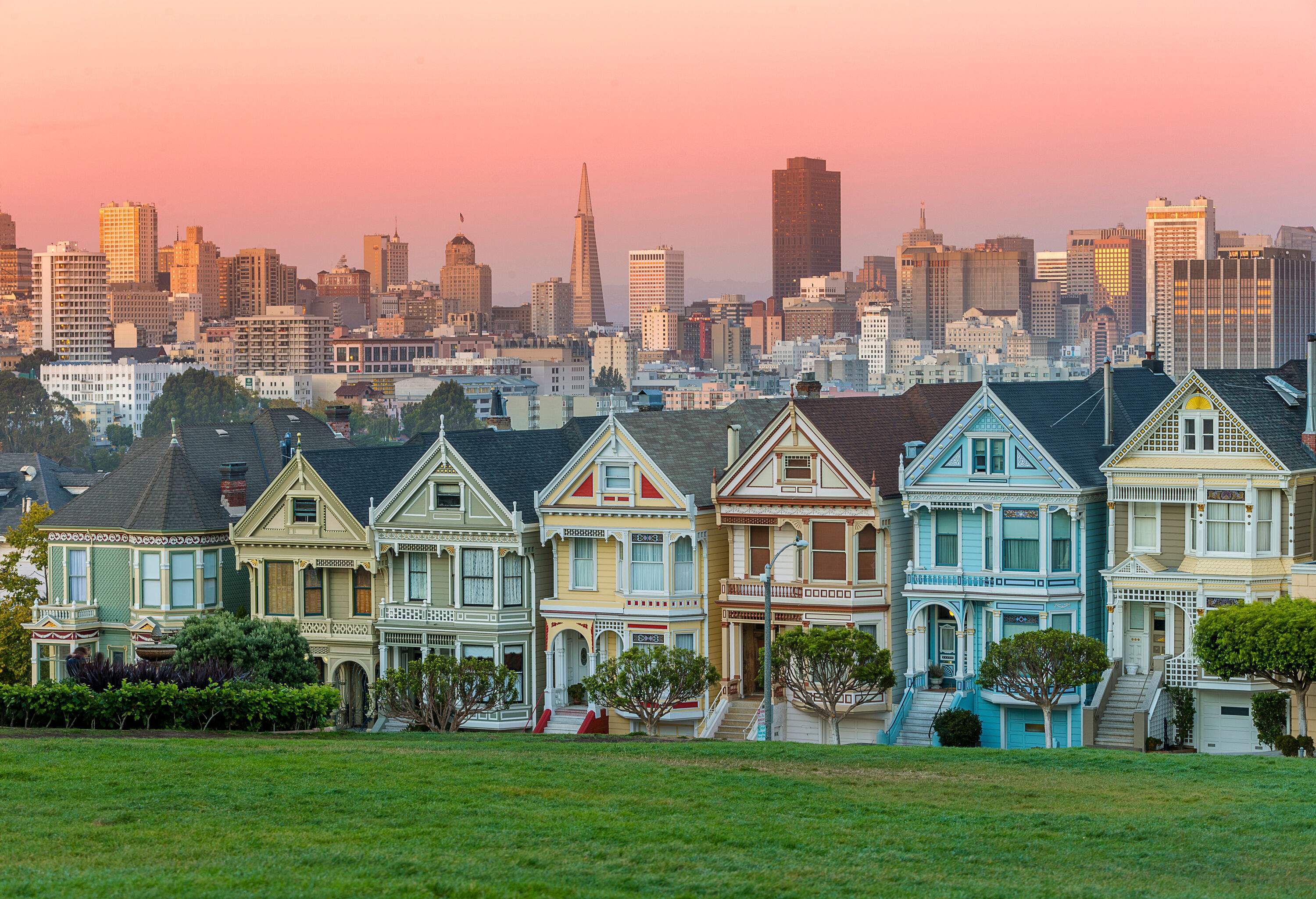 A lush green turf guides the eye towards a row of vibrant, colourful houses, as the distant city skyline adds a touch of urban charm to the picturesque scene.