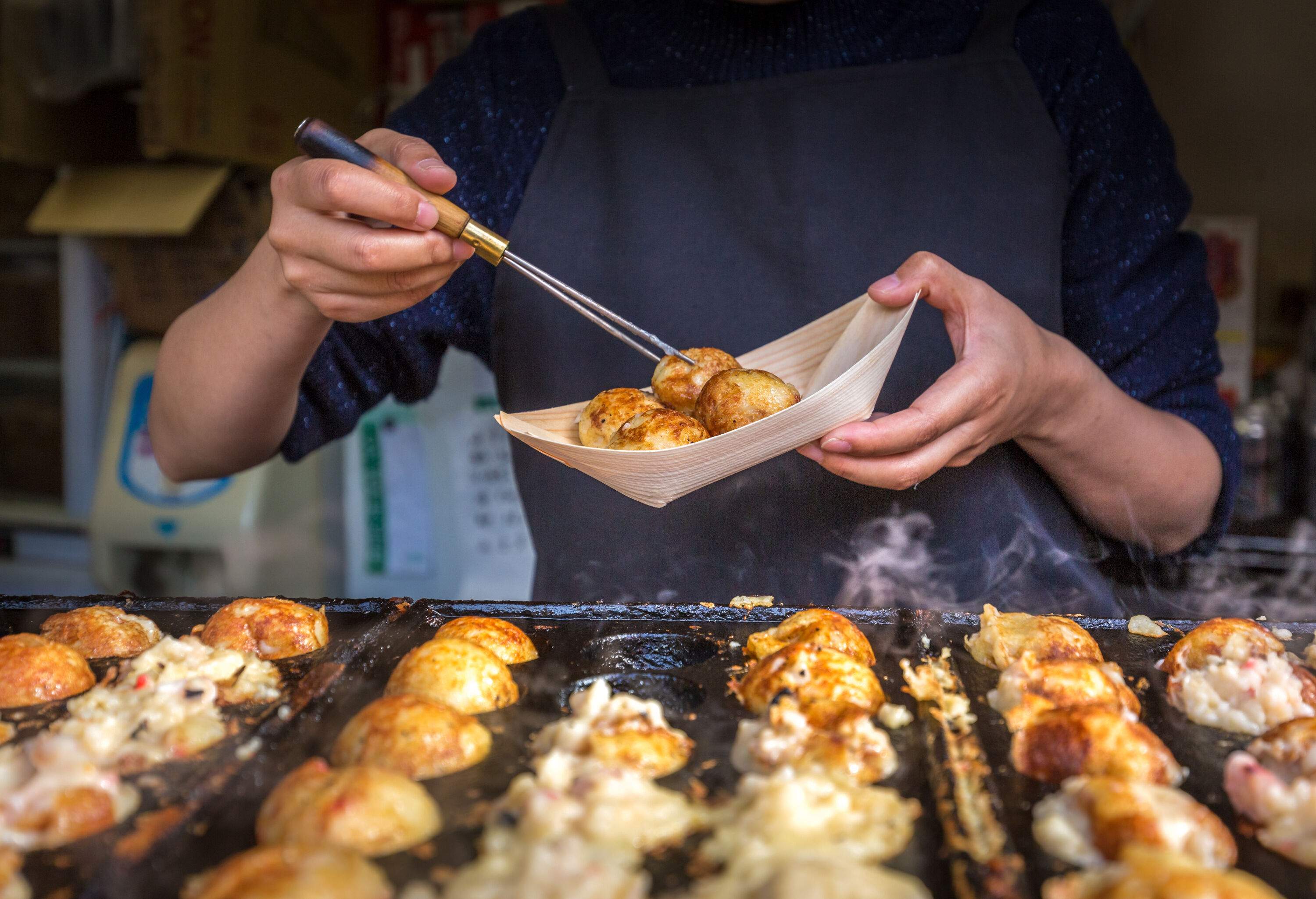 A person holds a chopstick and cooks Takoyaki in a hot pan.