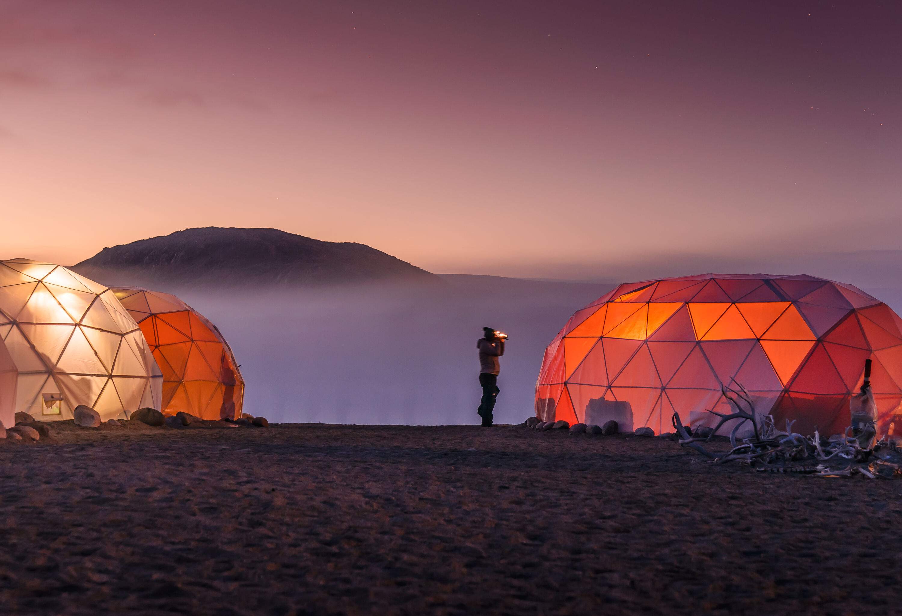 Dome tents in the mountains glowing from the inside against the night sky.