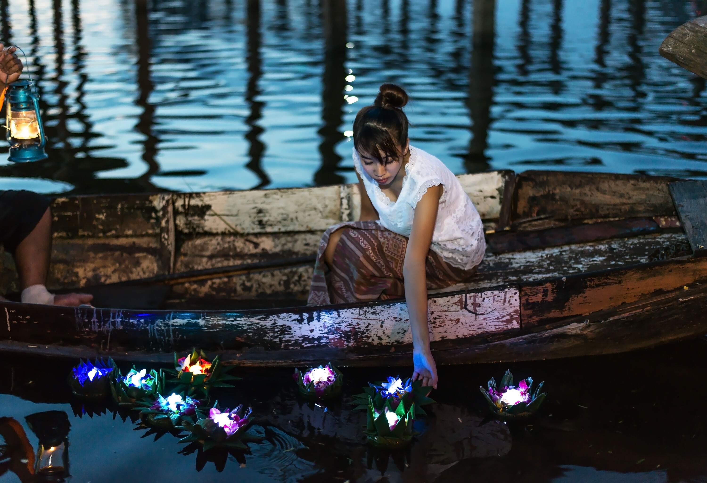 A woman on a boat launching colourful floating flower lanterns into the river.