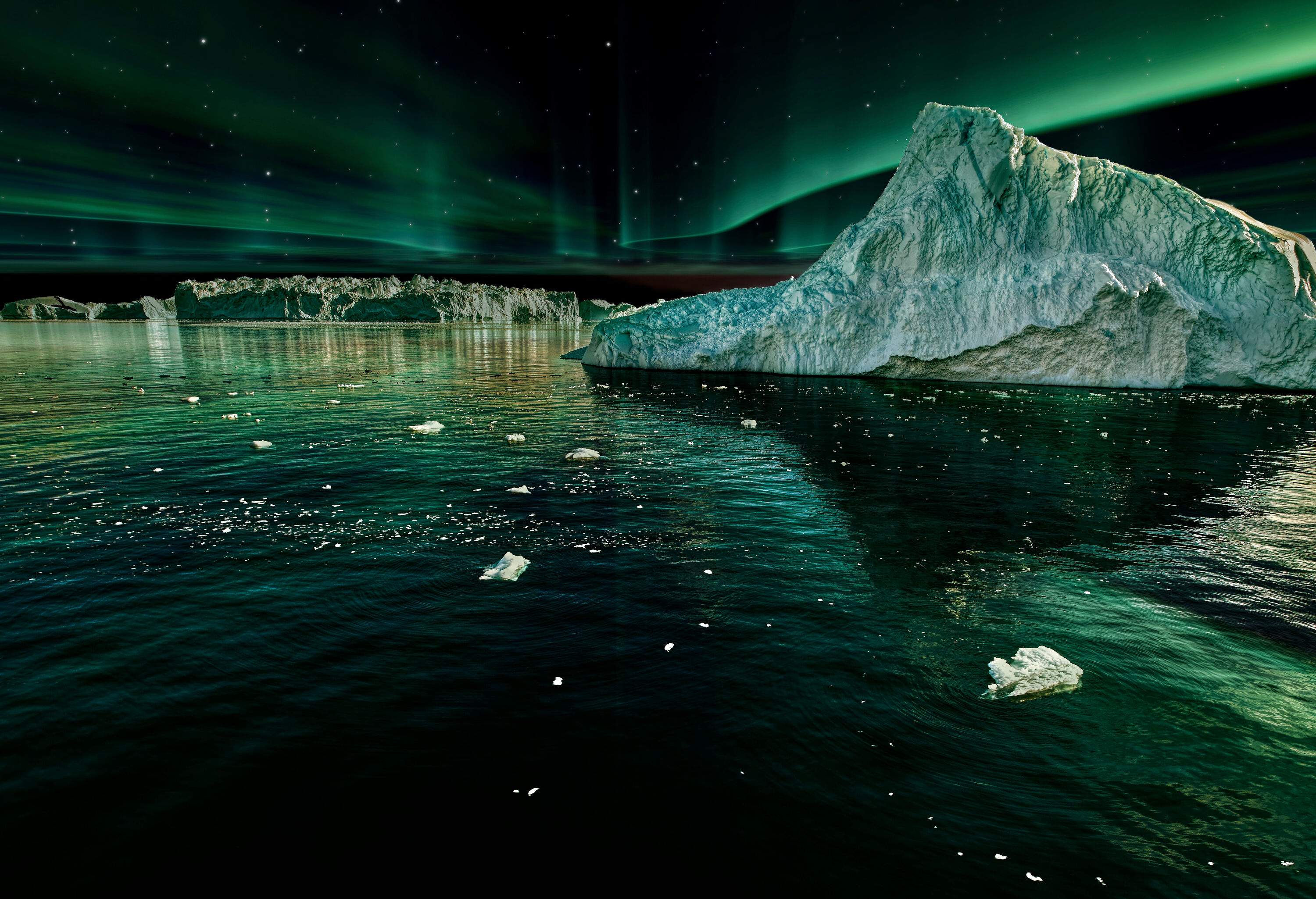 The tip of an iceberg emerges on the water's surface against the green and purple Northern lights dancing across the sky.