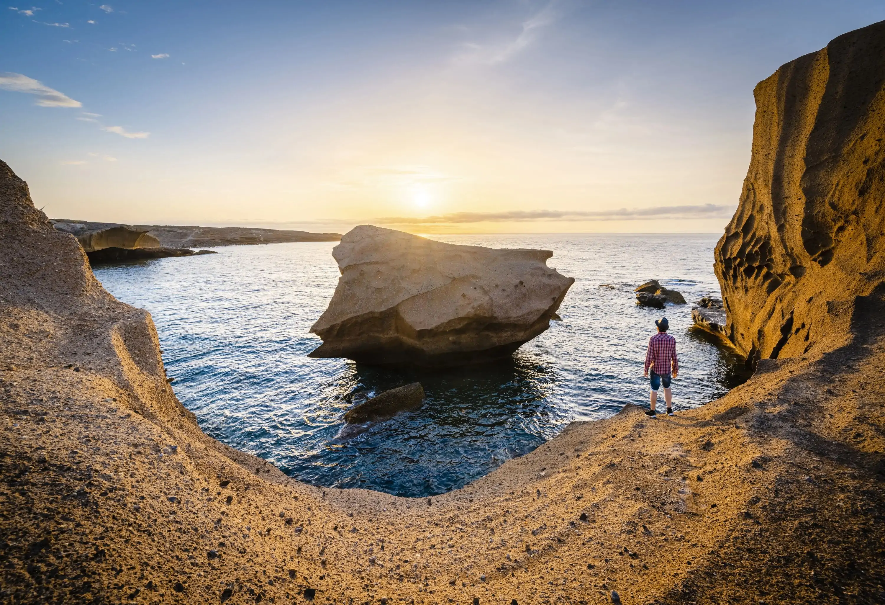 A man standing on the shore, watching the sun shine over the sea.