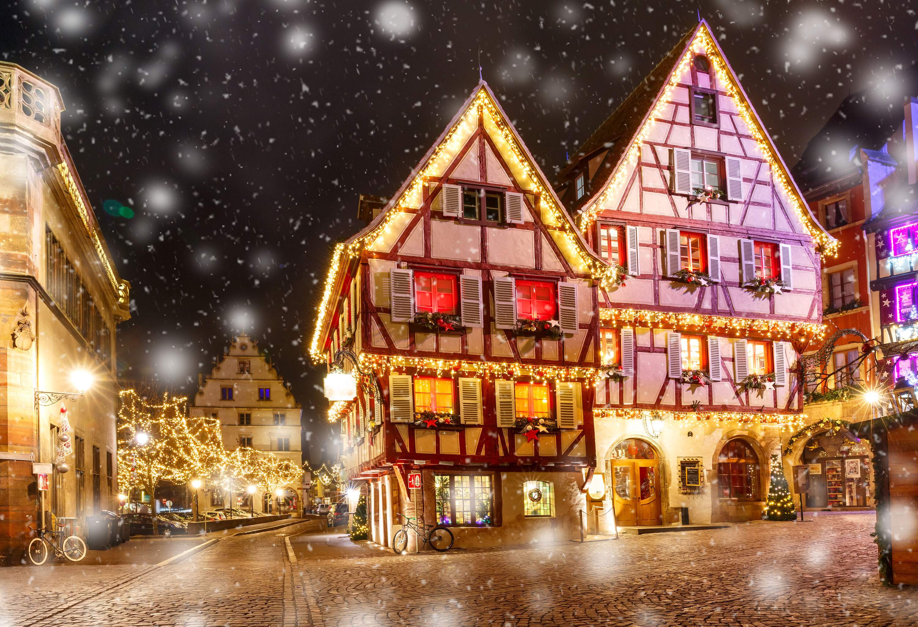 A street of traditional old half-timbered houses decorated with colourful Christmas lights and various Christmas ornaments on a snowy winter night.