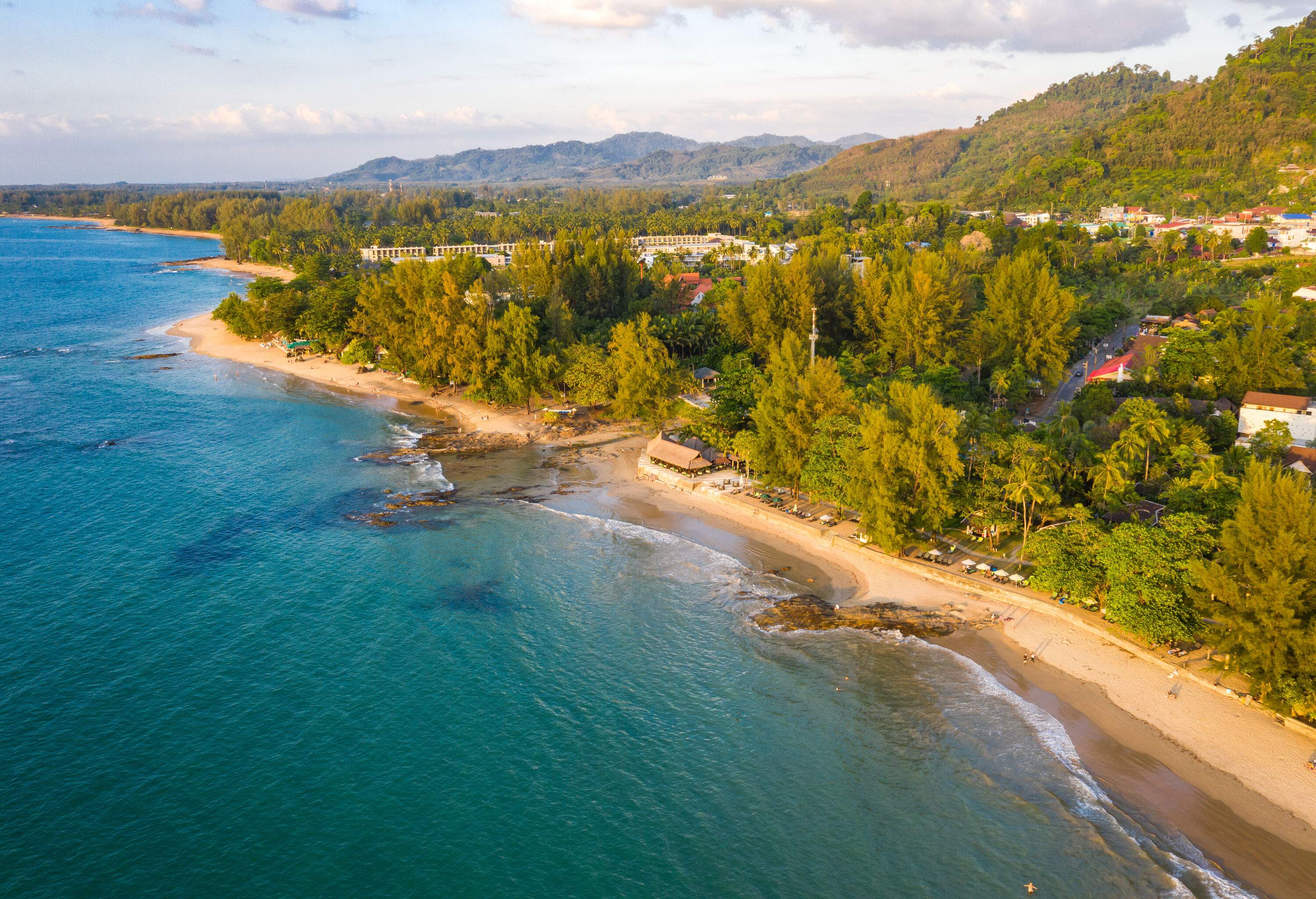 A narrow beach bordered by a lush wooded landscape, with towering tree-covered slopes stretching into the distance.