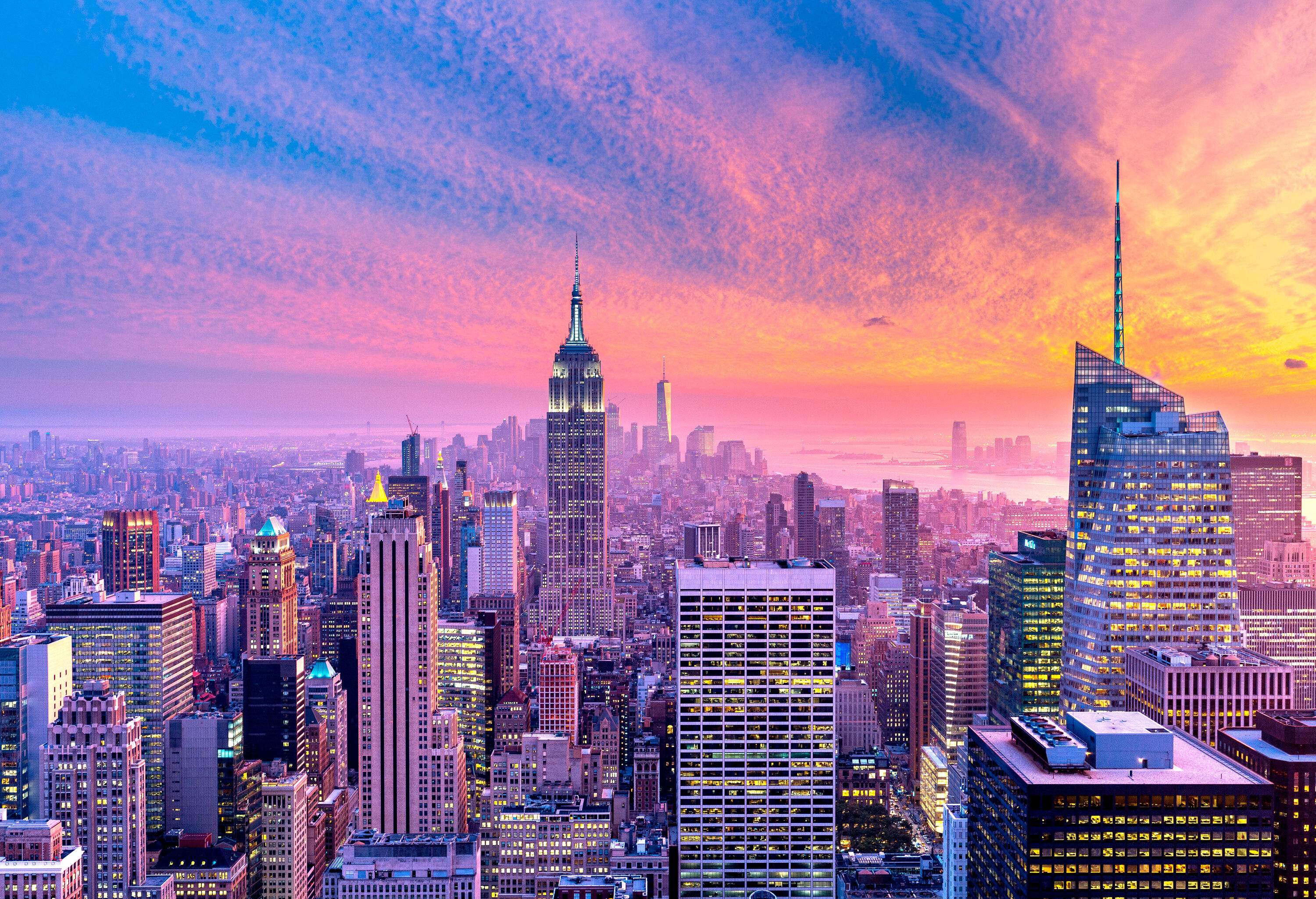 The scenic sunset gives vibrant colour to the sky above a crowded city dominated by tall buildings.