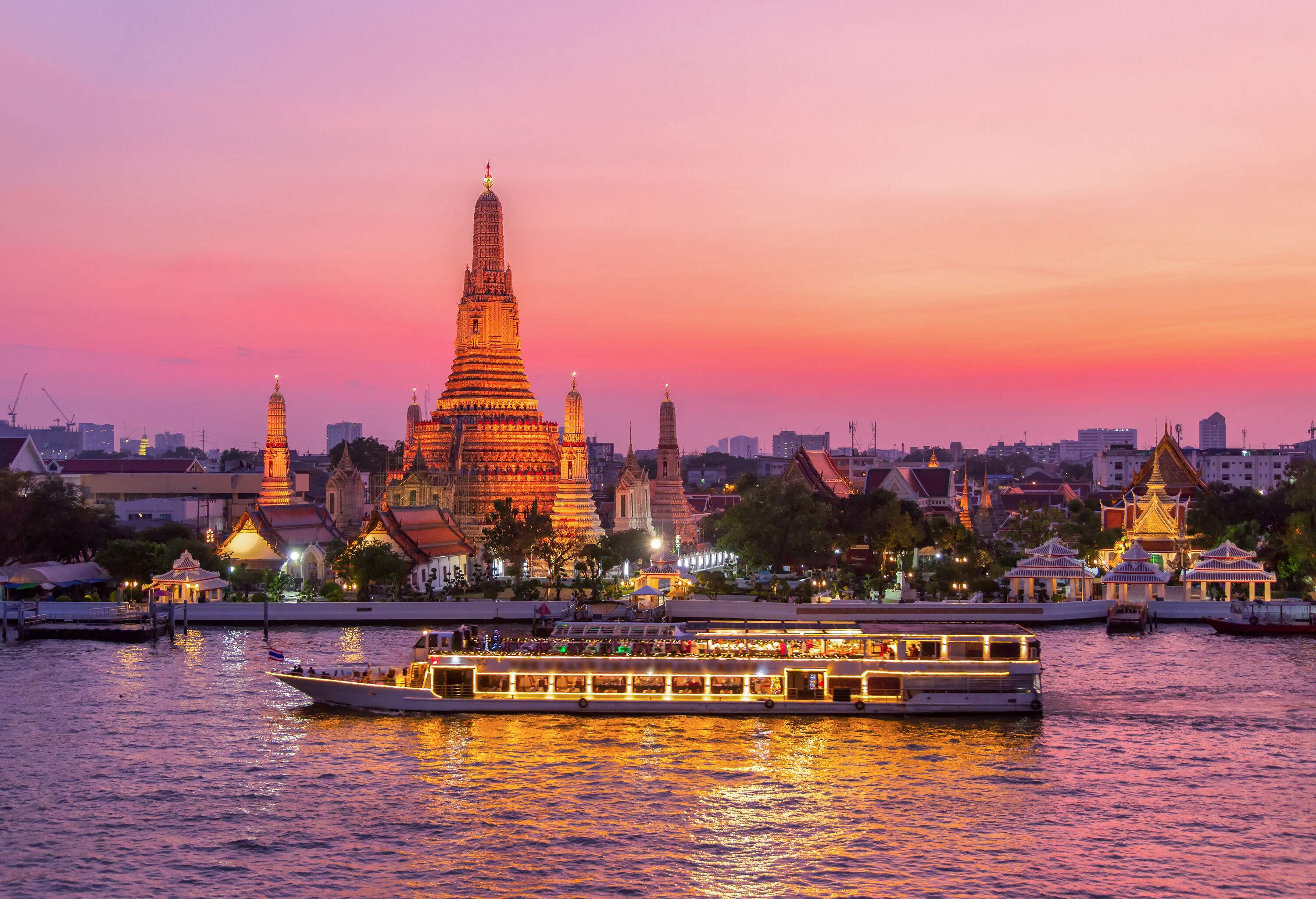 A cruise ship with passengers passing by the famous Wat Arun across the river.