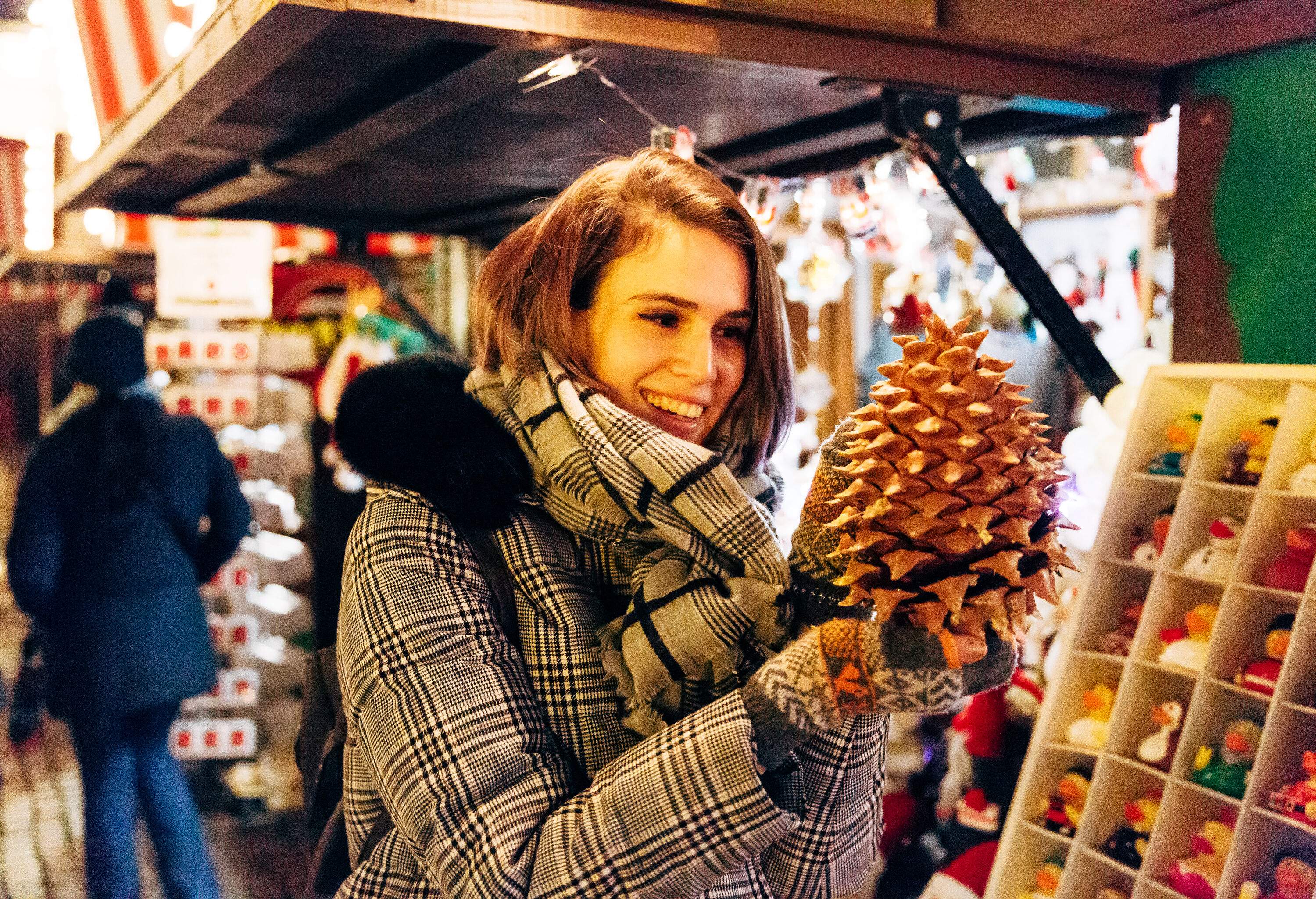 Woman smiling looking at large pine cone Christmas decoration at seasonal market