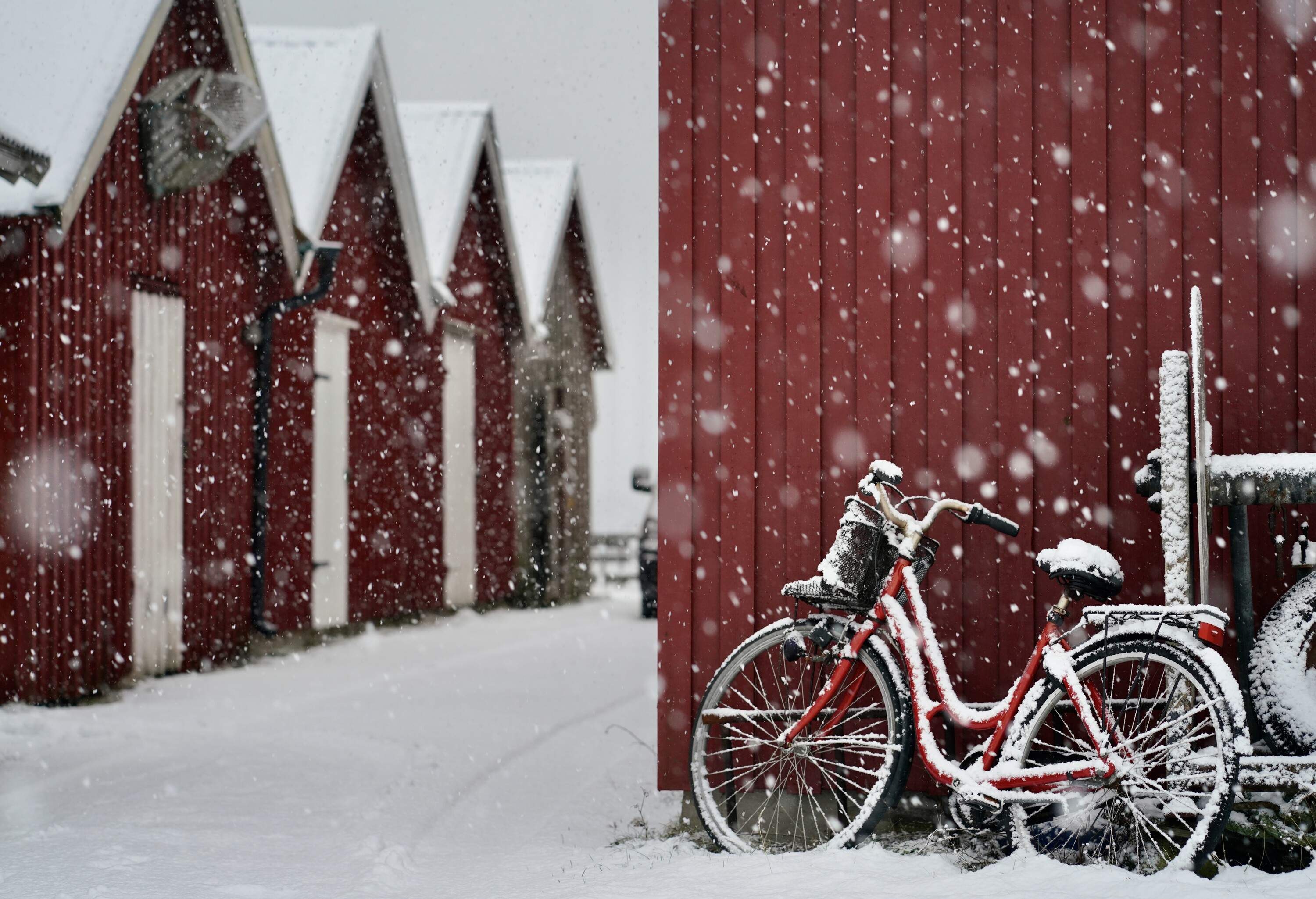 A row of traditional Swedish red huts with red bike parked on one side, on a grey winter snowy day