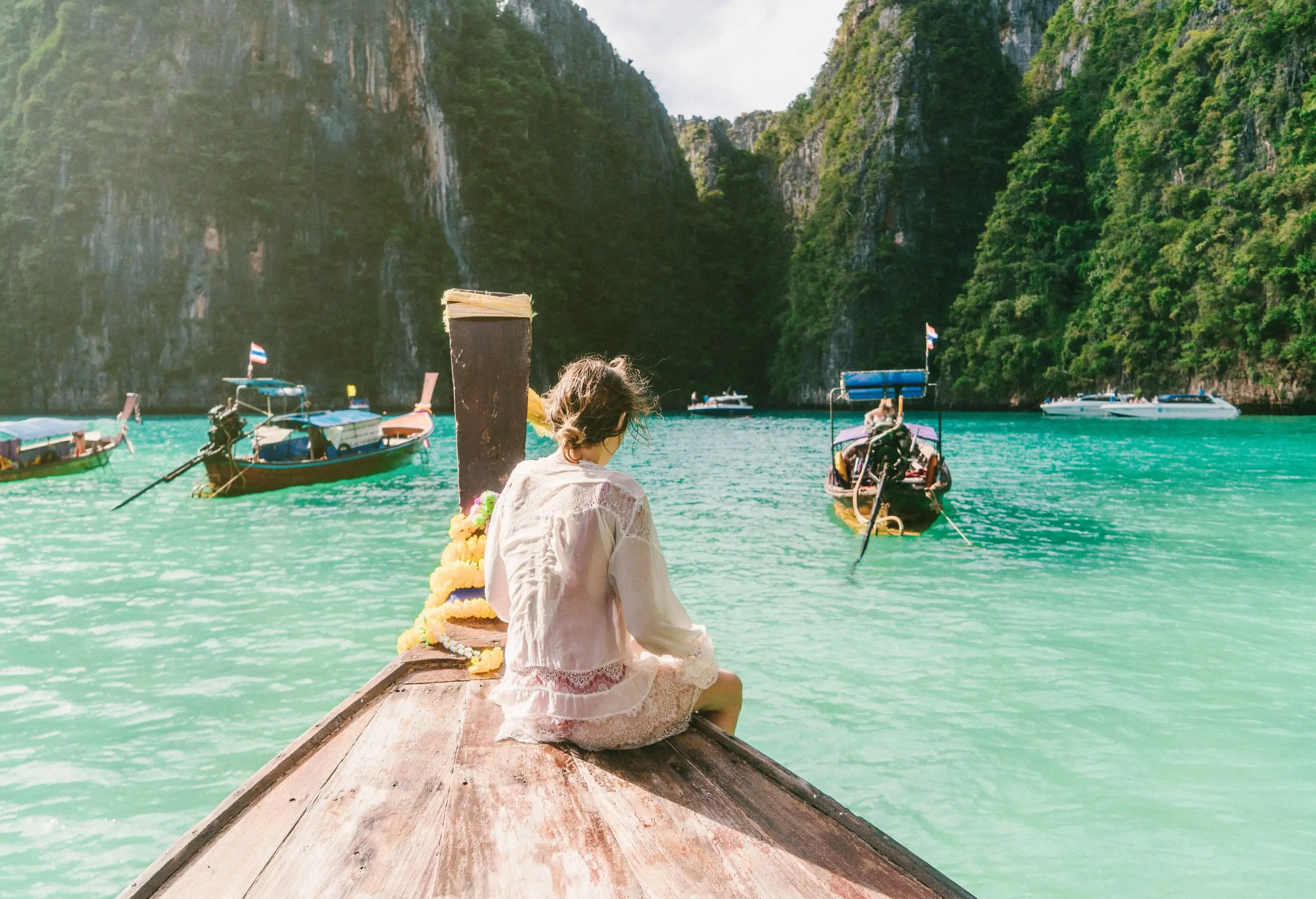 A woman sitting on the prow of a boat as it drifts in the sun-lit waters of a bay.