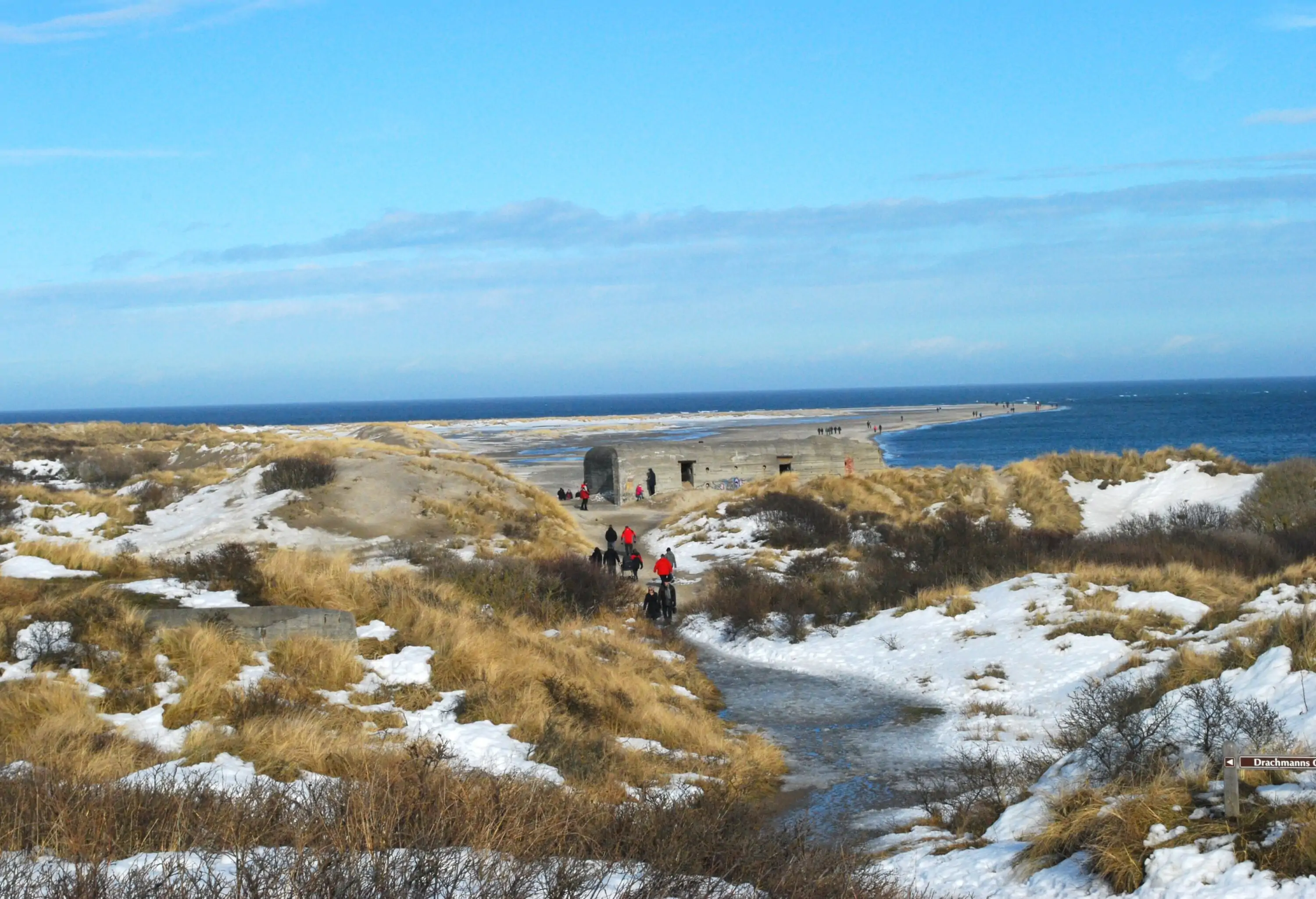 View of nordic beach on a sunny winter day, snow on the ground and people in the background walking through sanddunes