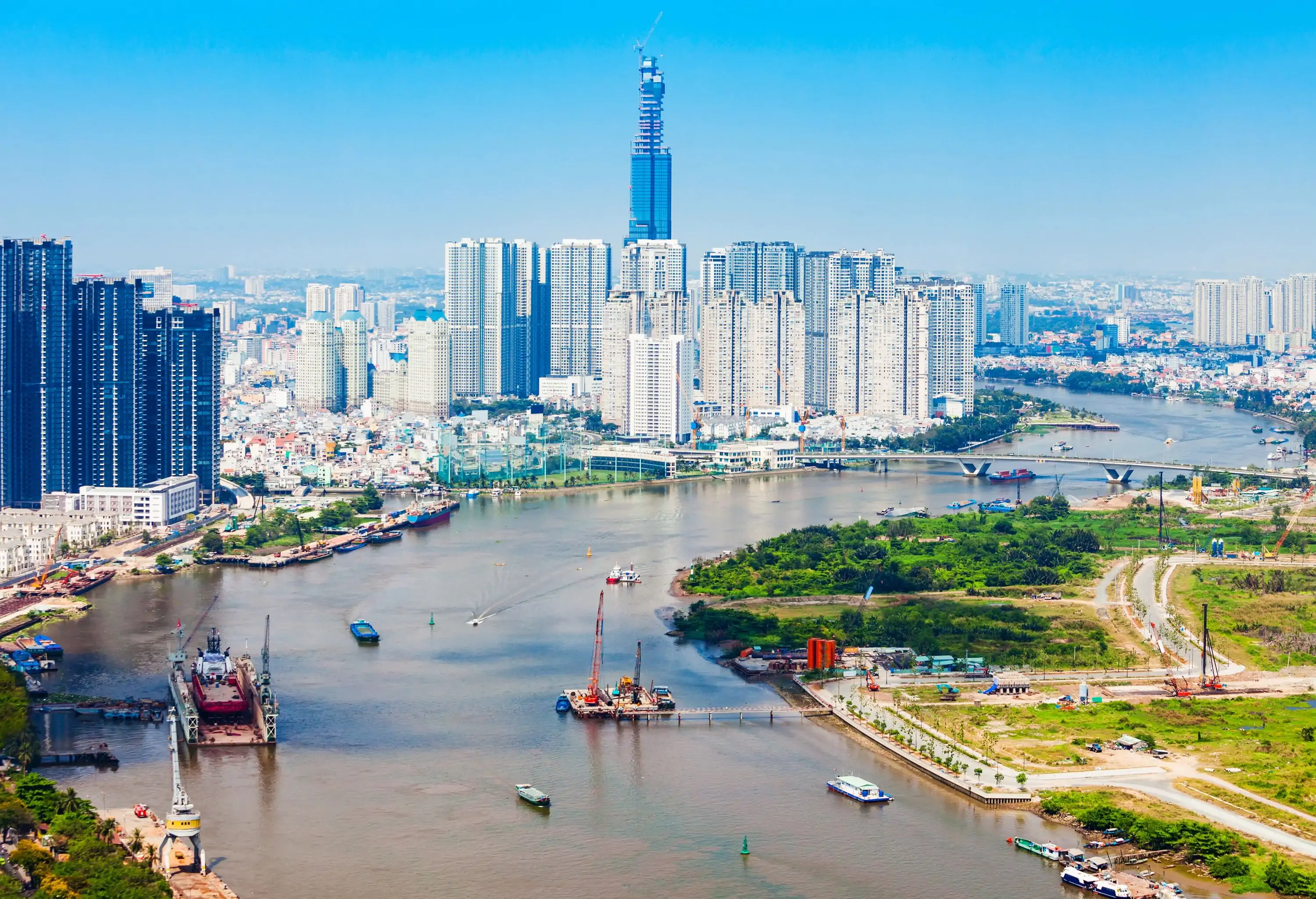 A wide river strewn with boats winding across a city surrounded by soaring skyscrapers.