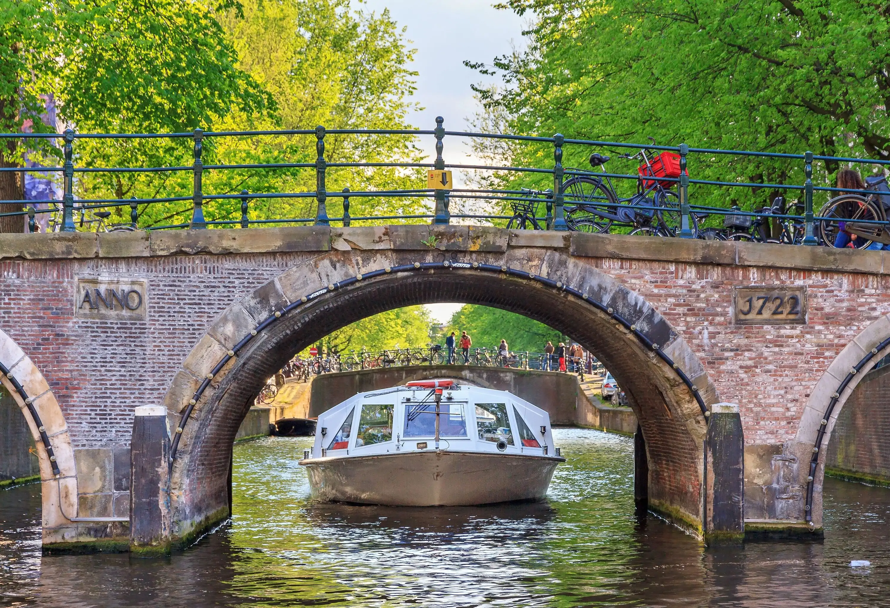 Canal cruise boat goes under the bridge over the Leidse canal at the Patricians' or Lords' canal (Herengracht) in Amsterdam in spring