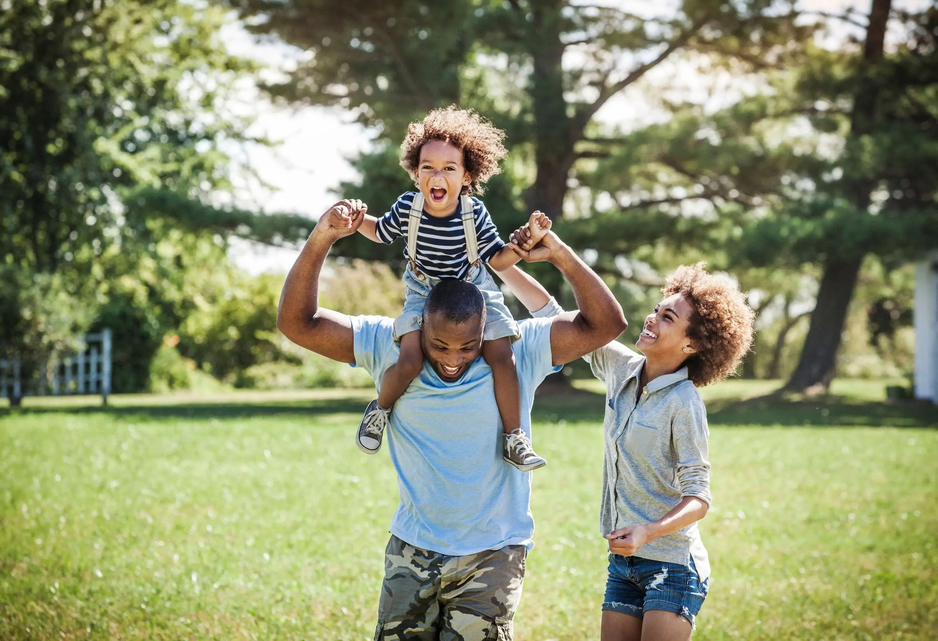 A kid having fun riding on his father's shoulders as the mother watches on.