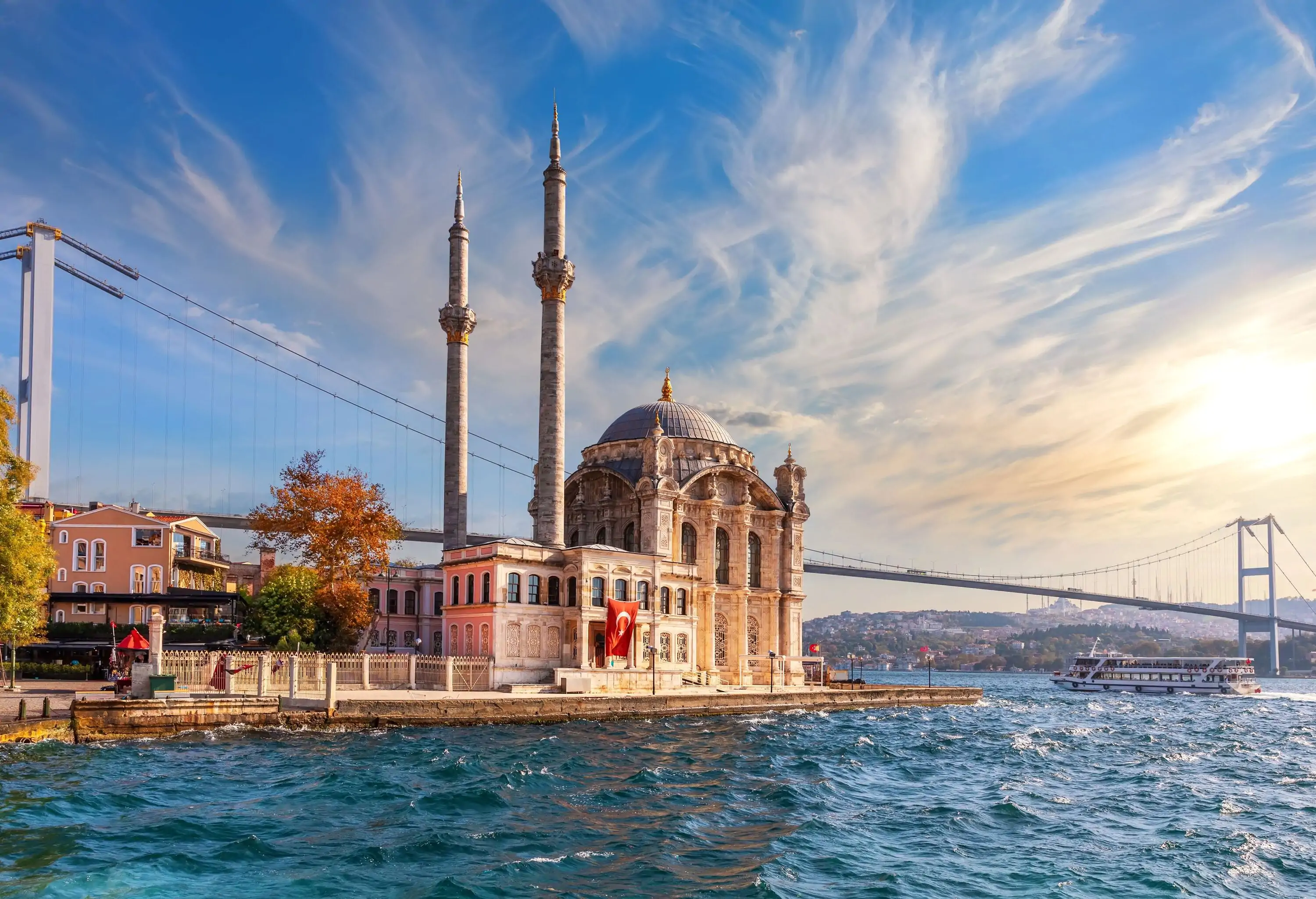 A waterside domed mosque with a long suspension bridge running behind it.