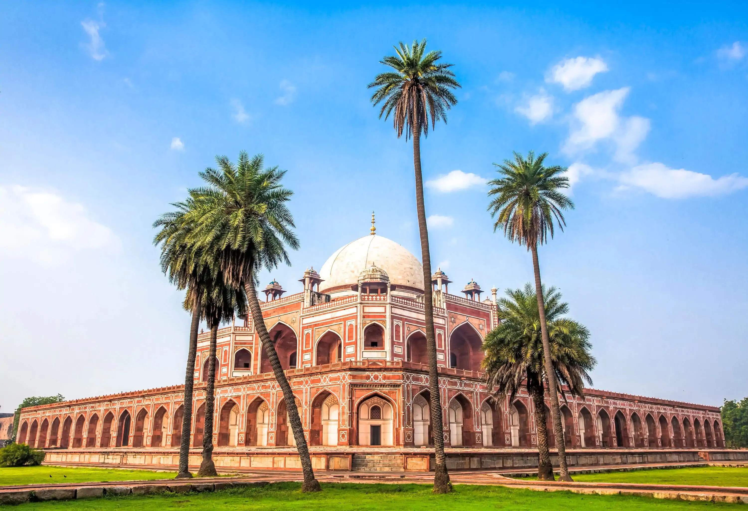 A sunlit vista of the majestic Humayun's Tomb, featuring intricate red sandstone and white marble details, is framed by soaring palm trees and a serene atmosphere.