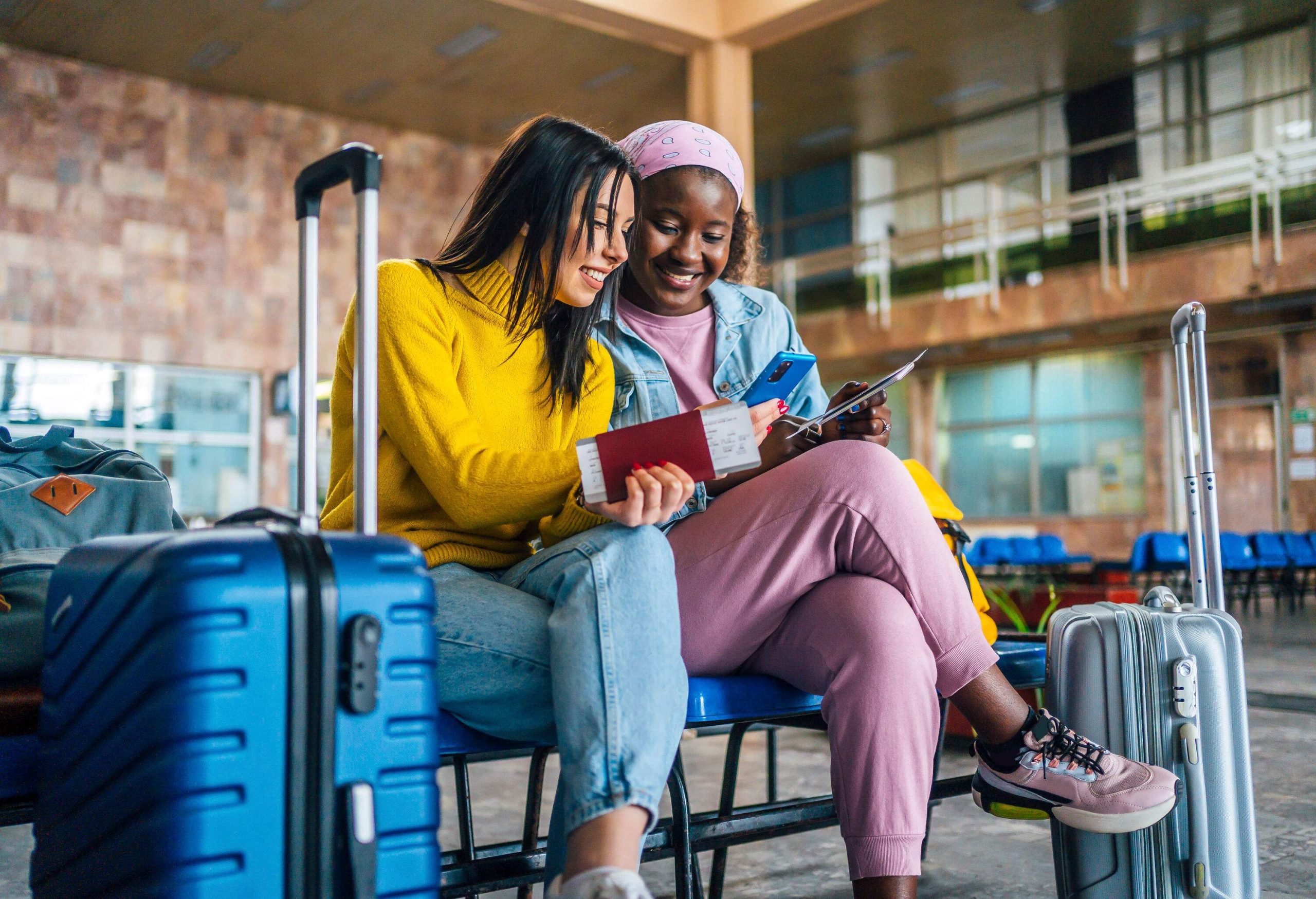 Young cheerful multi racial women friends looking at mobile phone at the airport while waiting for their flight