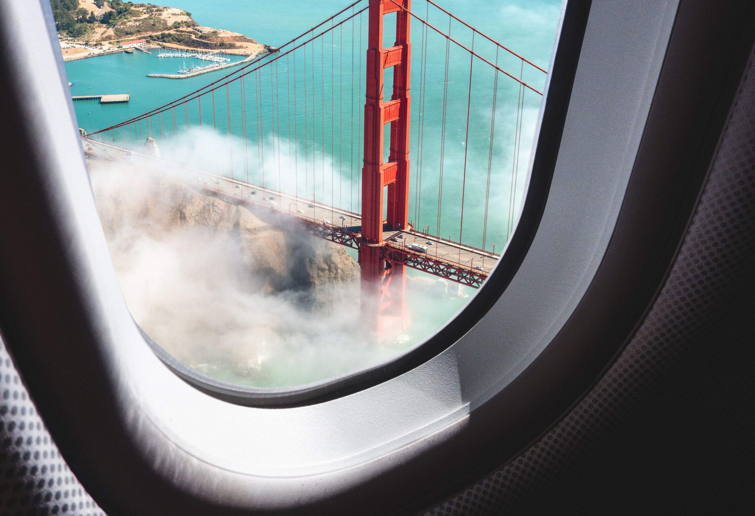 An airplane window view of a suspension bridge shrouded in thick fog.