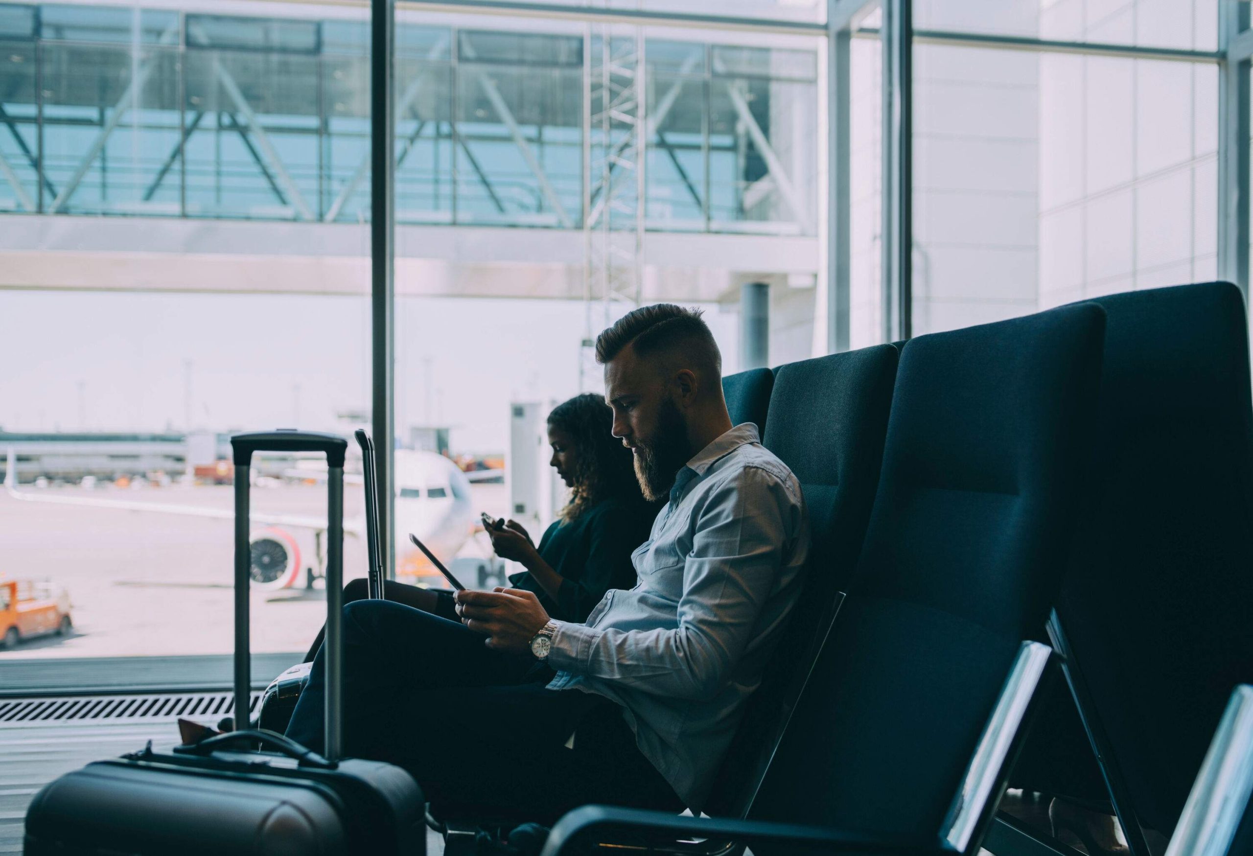 Two people seated in an airport departure lounge engaged with their smartphones.