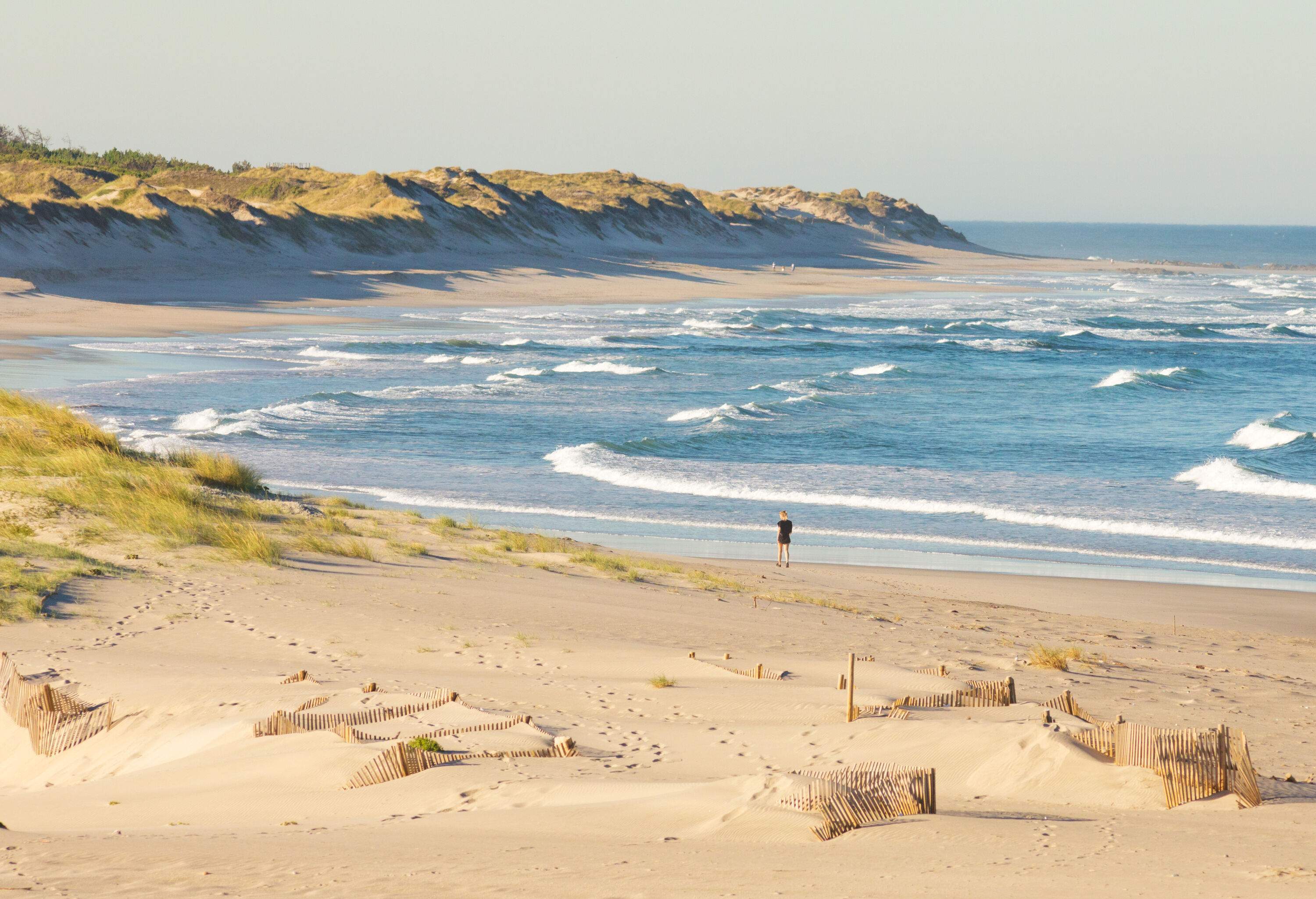 A girl strolls alone on Cabedelo Beach in the morning, enjoying the gentle sound of waves as they lap against the shore.