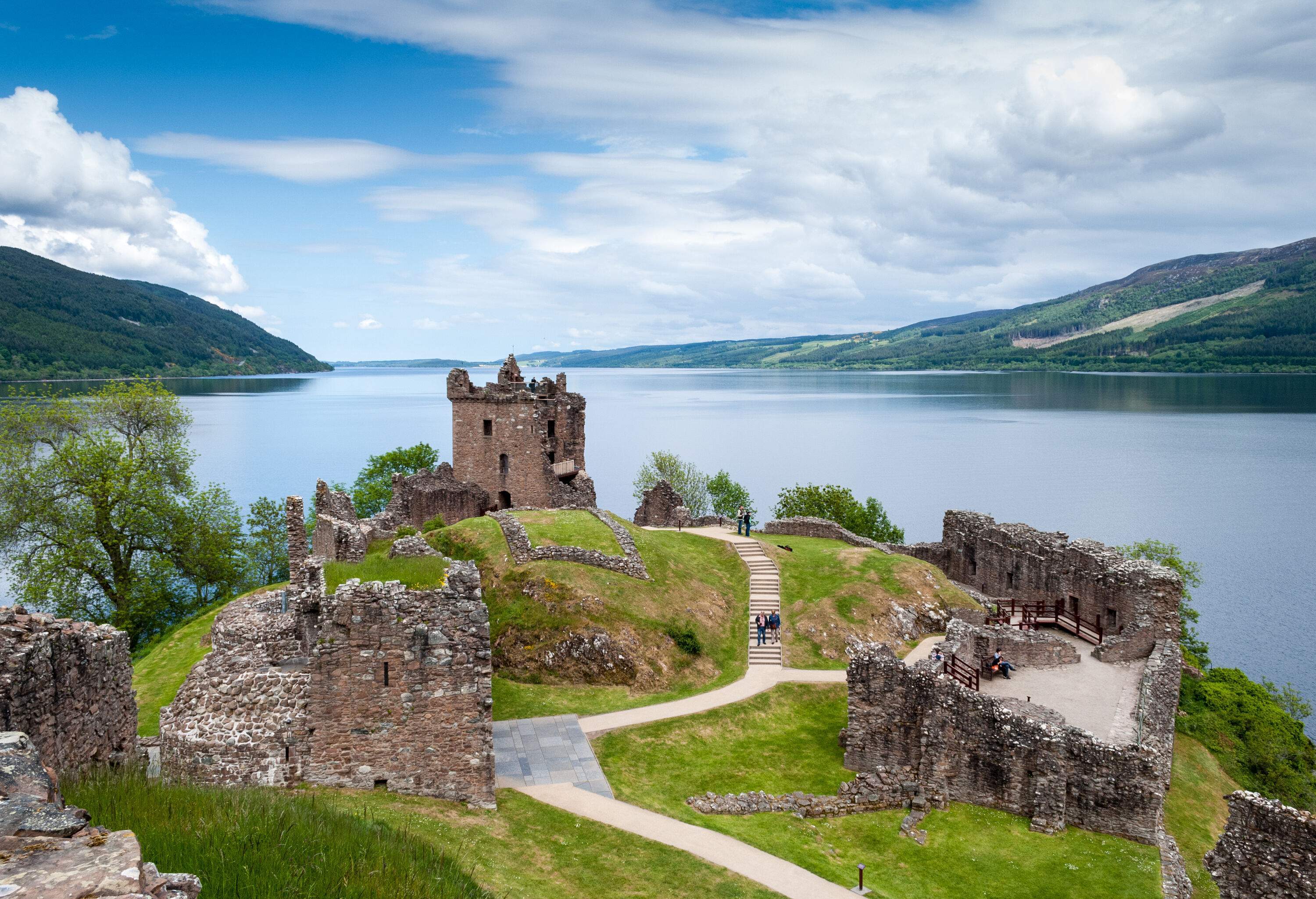 Ruins of a fortified stone castle perched on a hill above a lake.