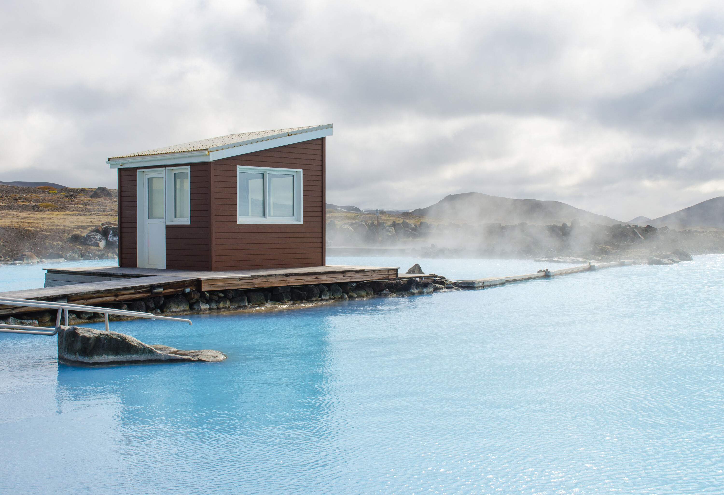 A brown cabin at the centre of a lake's steaming pool.