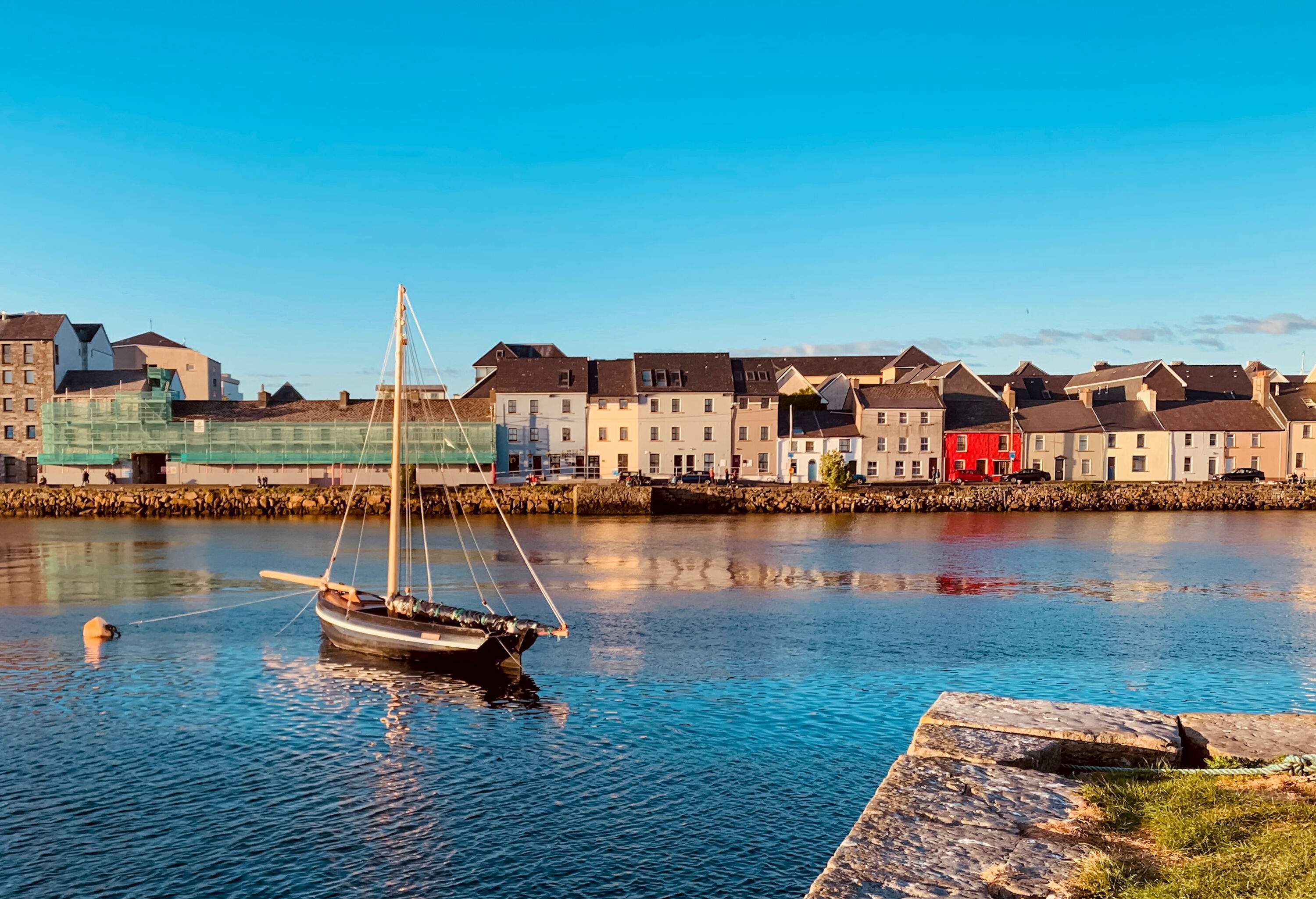 A lone boat moored in the bay lined with traditional buildings with brown roofs.