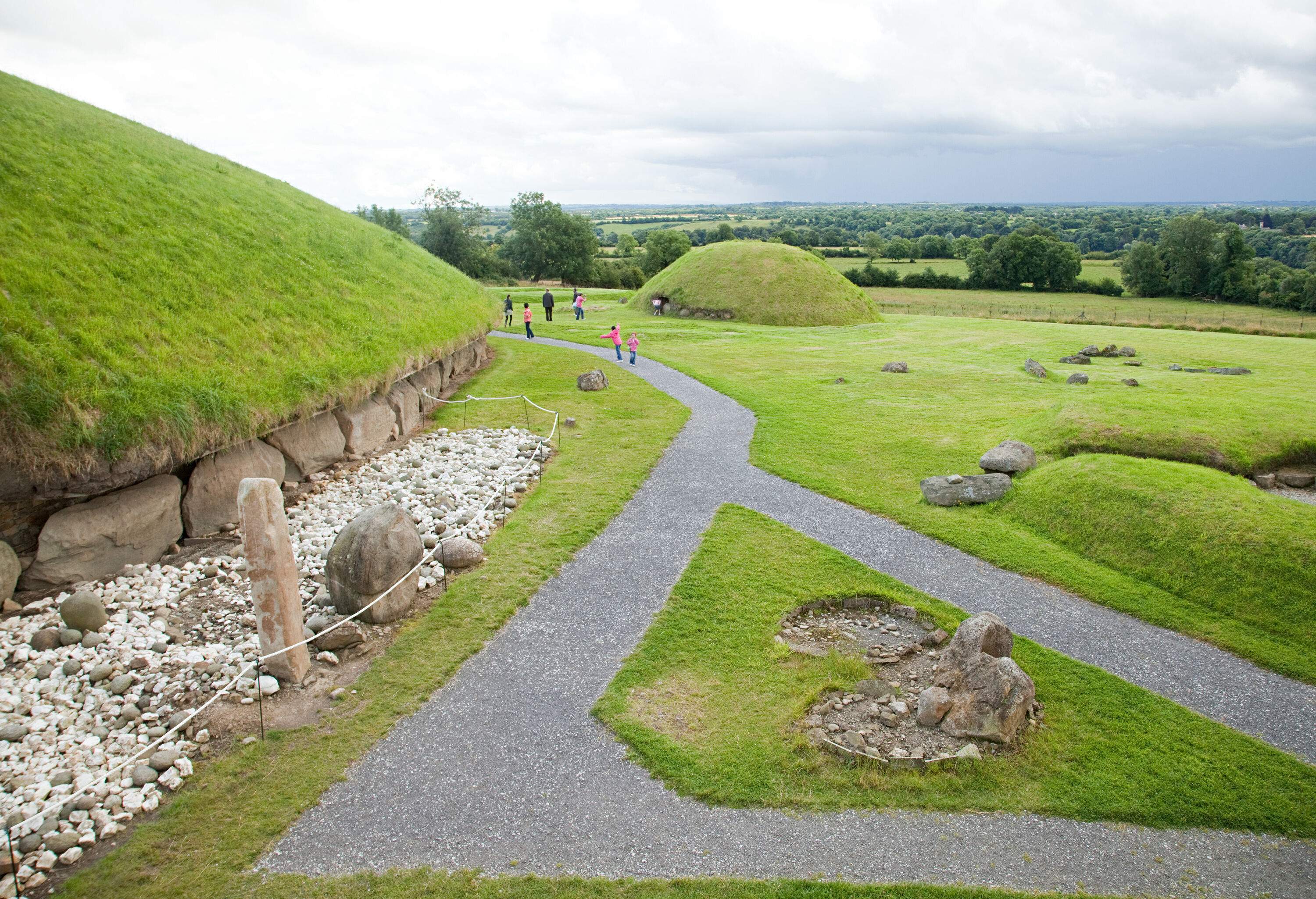 A small path across a green lawn with mounds covered in grass.