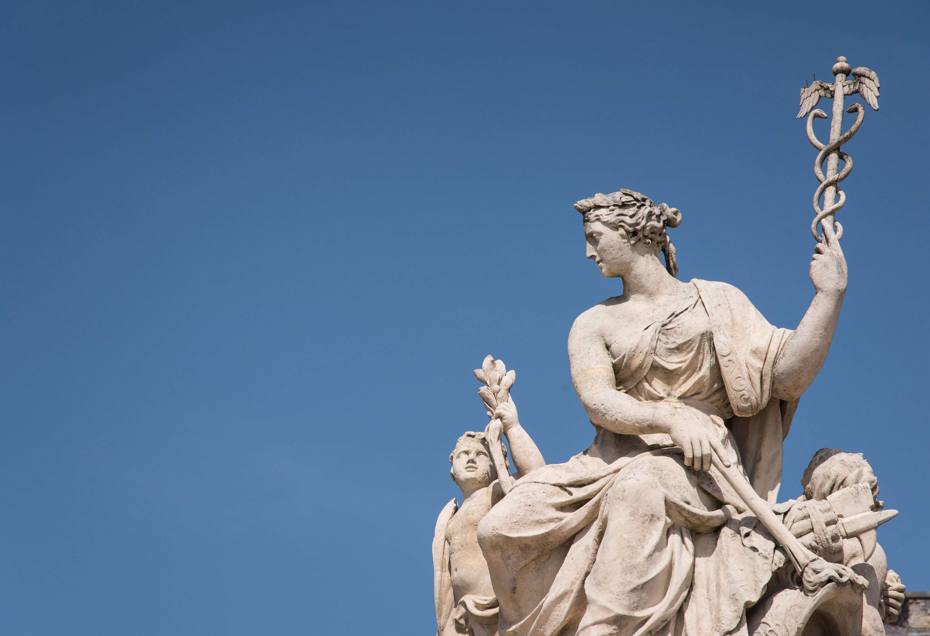 A statue holding a caduceus against the clear blue sky.
