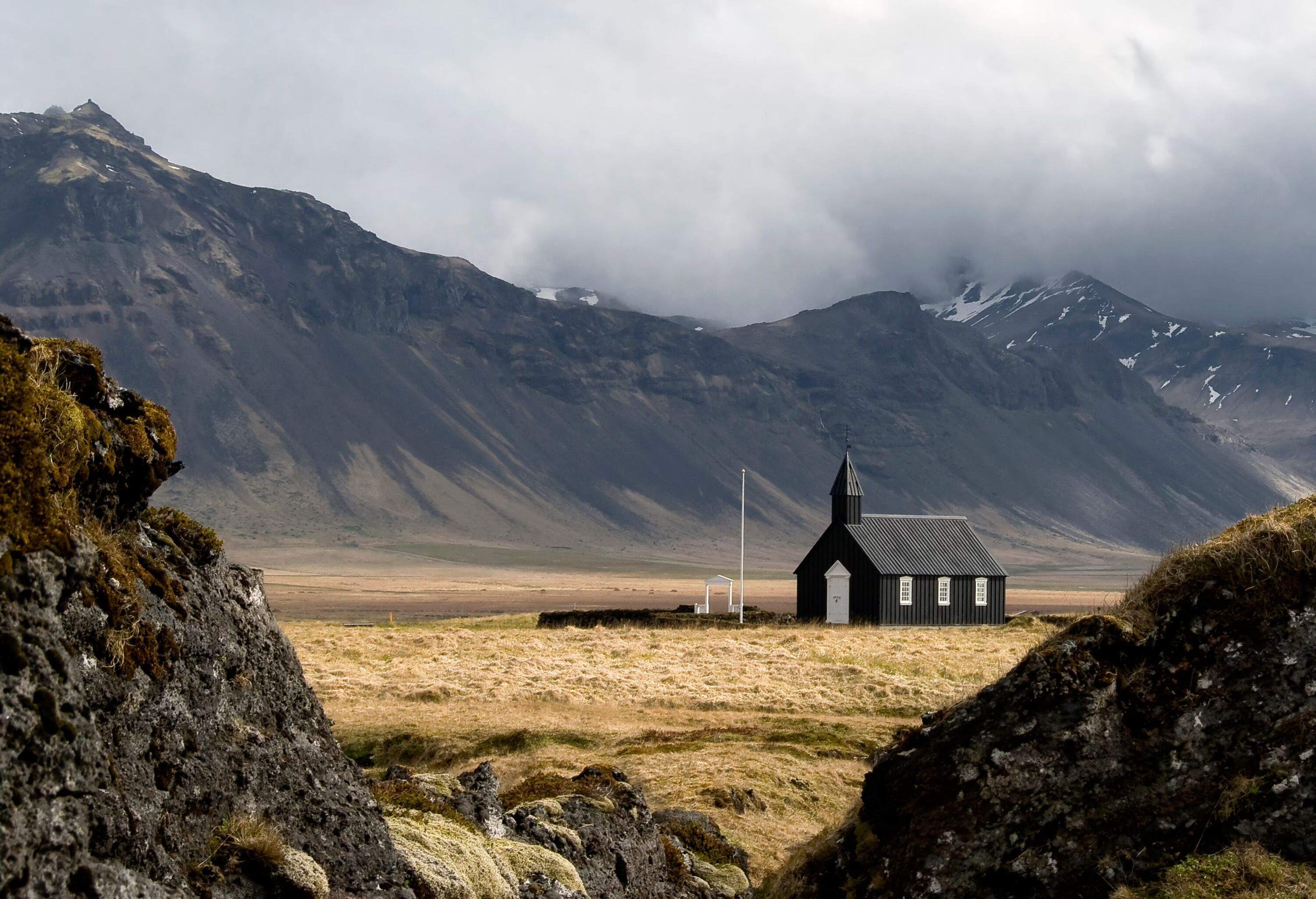 Traditional wooden Black Church at Búðir - Snæfellsnes Peninsula, Iceland against a rugged mountainous landscape