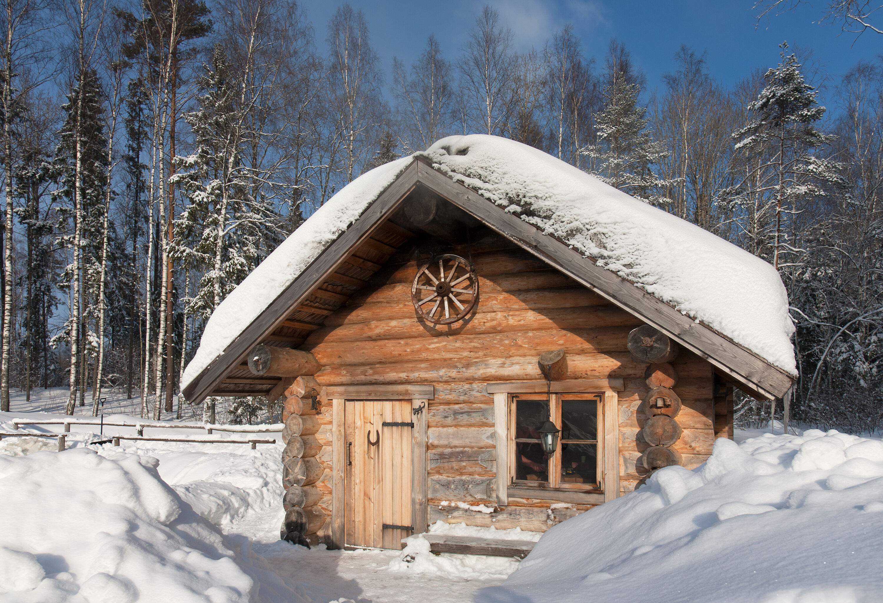 A wood cabin with heavy snow on the roof next to a frosted forest.