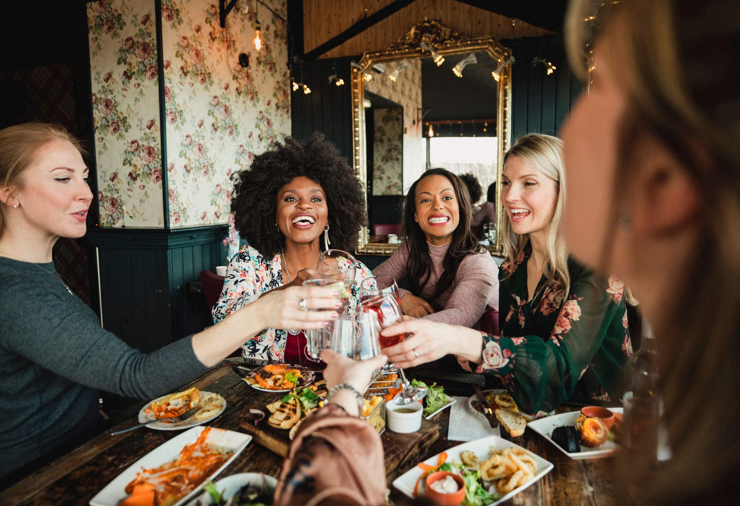 A group of women laughing as they raise their glasses over a table laden with delectable meals.