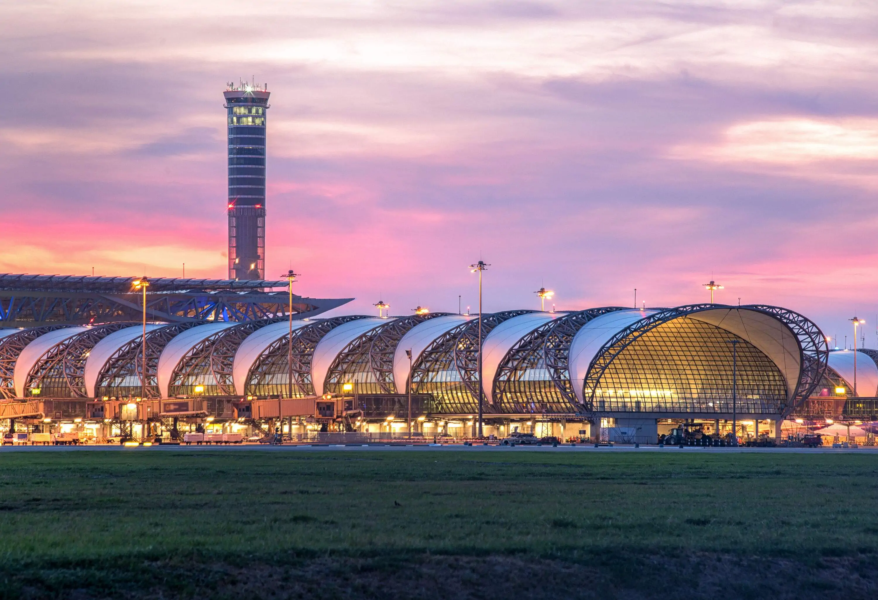 A glass-walled passenger terminal under a large roof trellis with a control tower in the background.